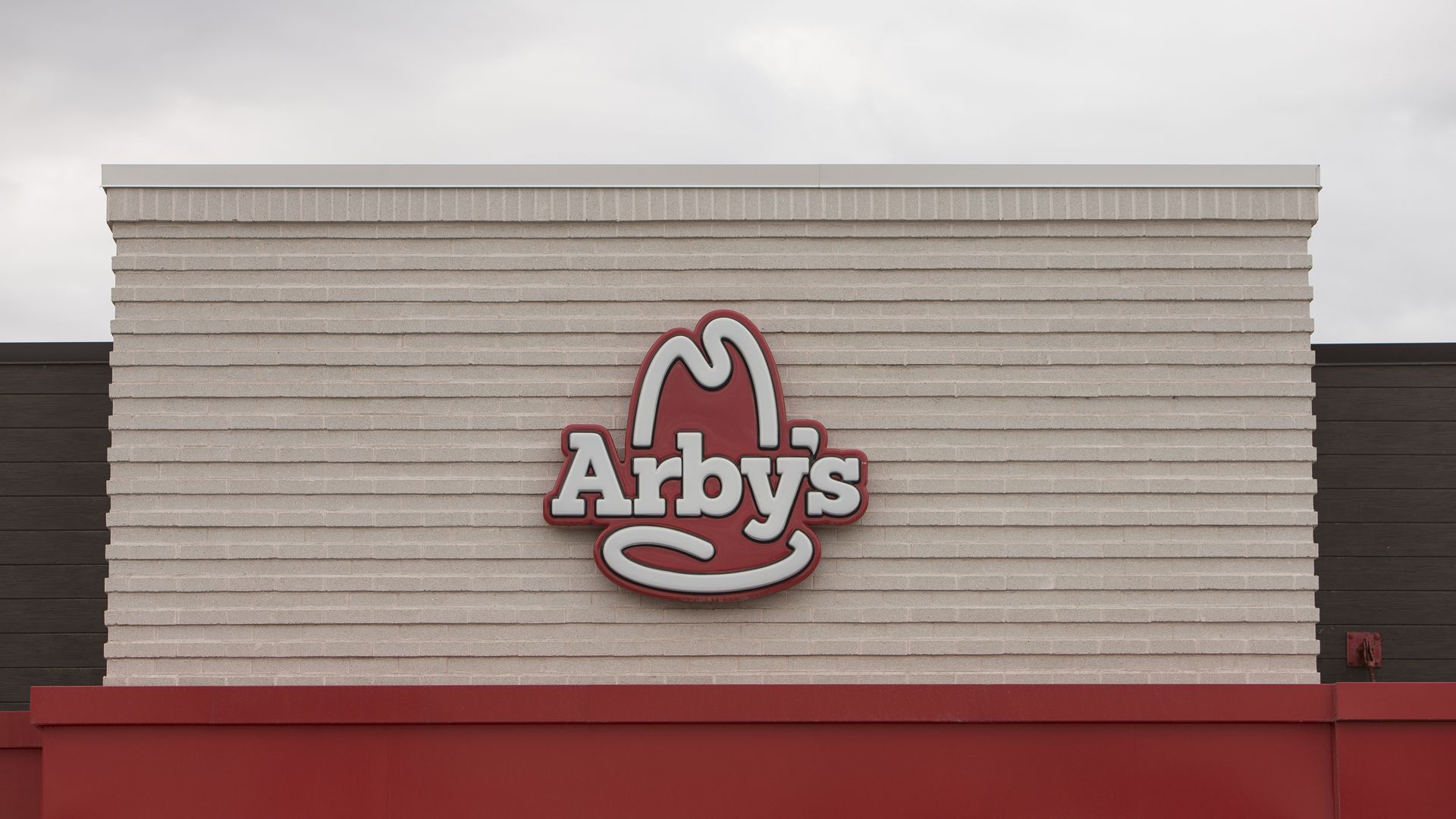 Red Arby's logo on biege building with grey skies.