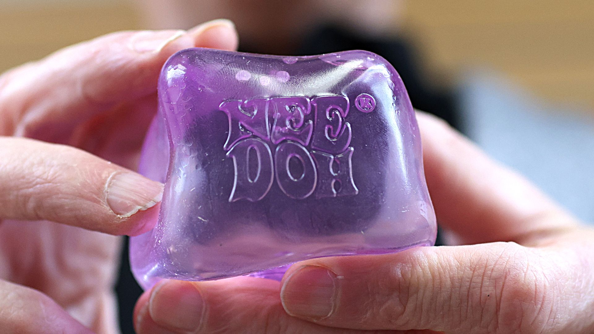 A person holds a purple, gelatinous-looking cube with a label that says NeeDoh.