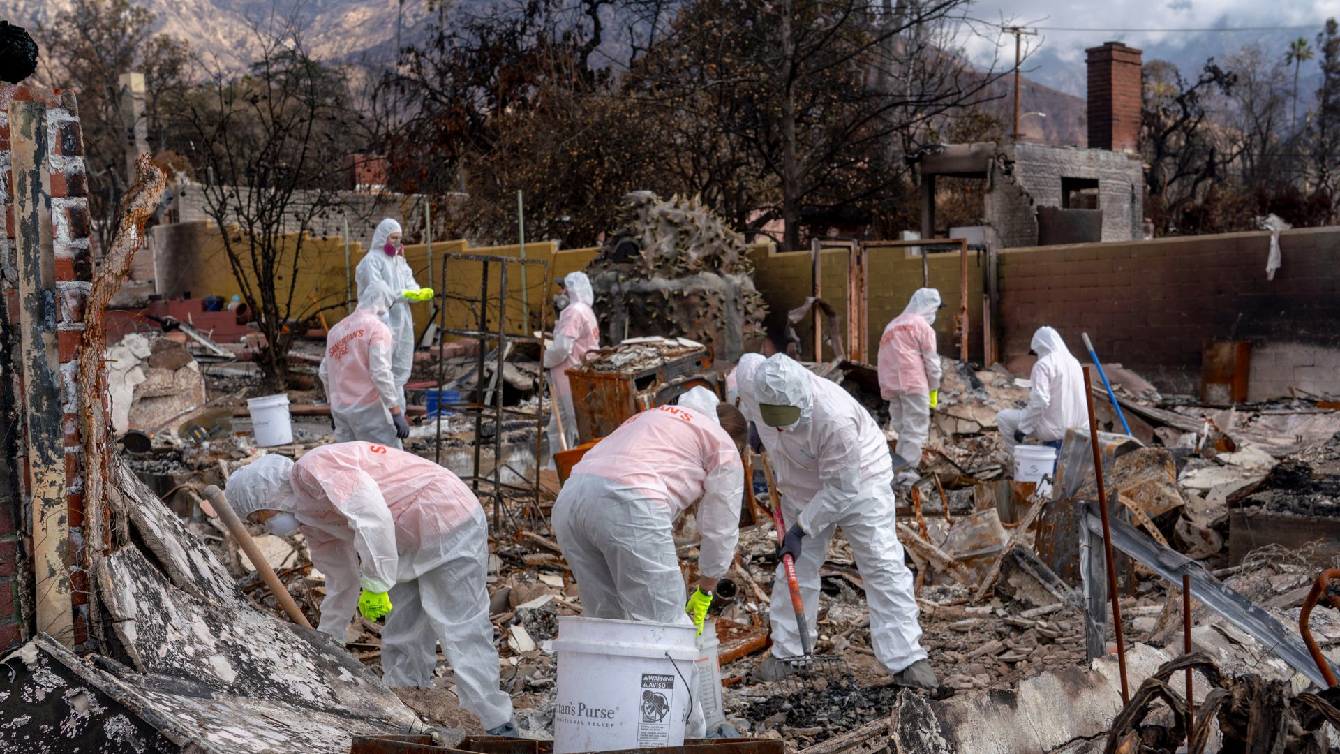 Contractors in protective gear remove debris by hand from a home incinerated by the Los Angeles wildfires.