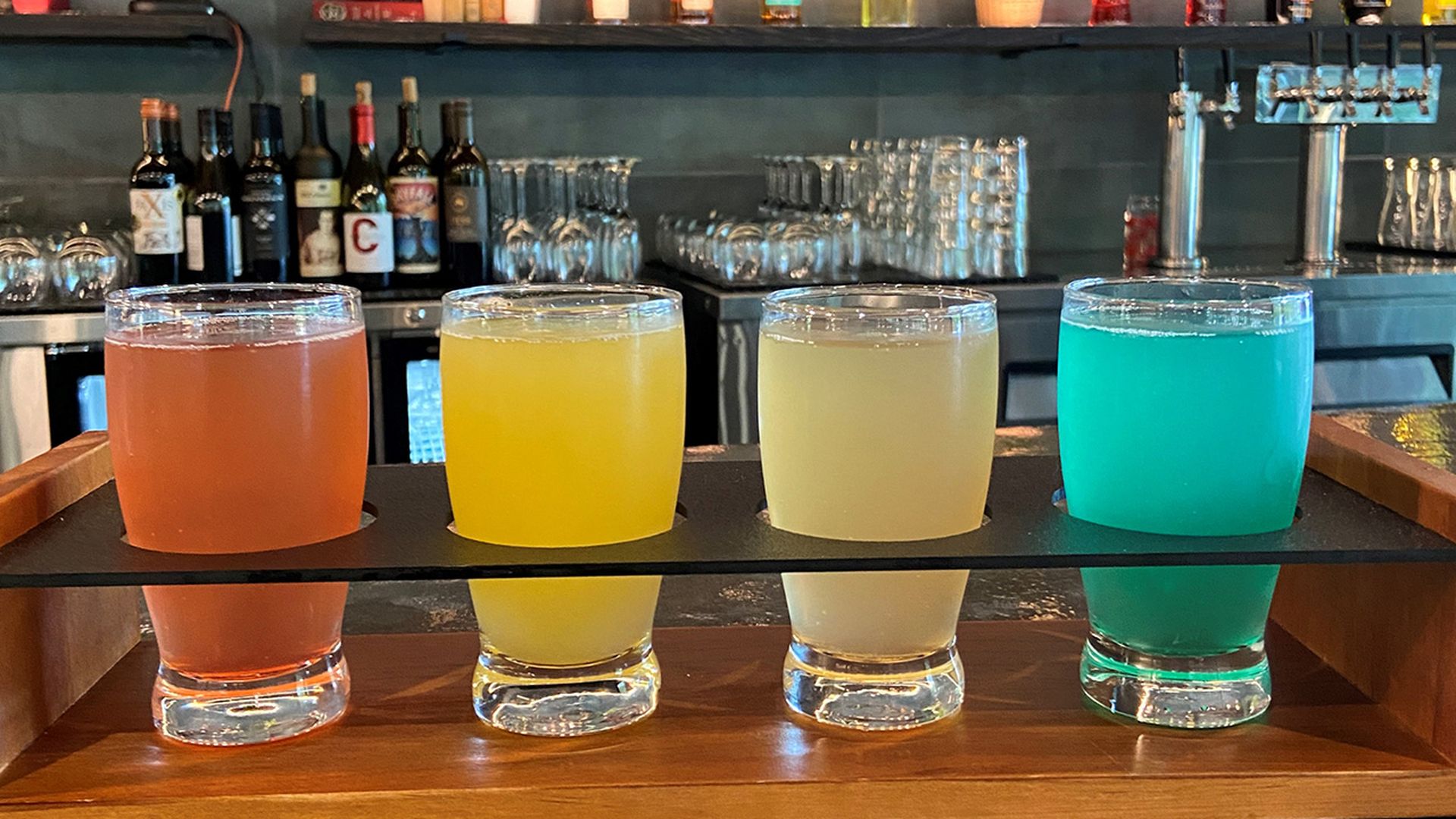 A four-mimosa flight on top of a bar counter with colors ranging from orange, yellow, beige and a turquoise-ish