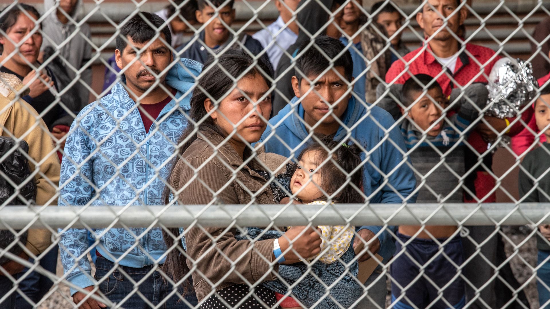 Migrants are gathered inside the fence of a makeshift detention center