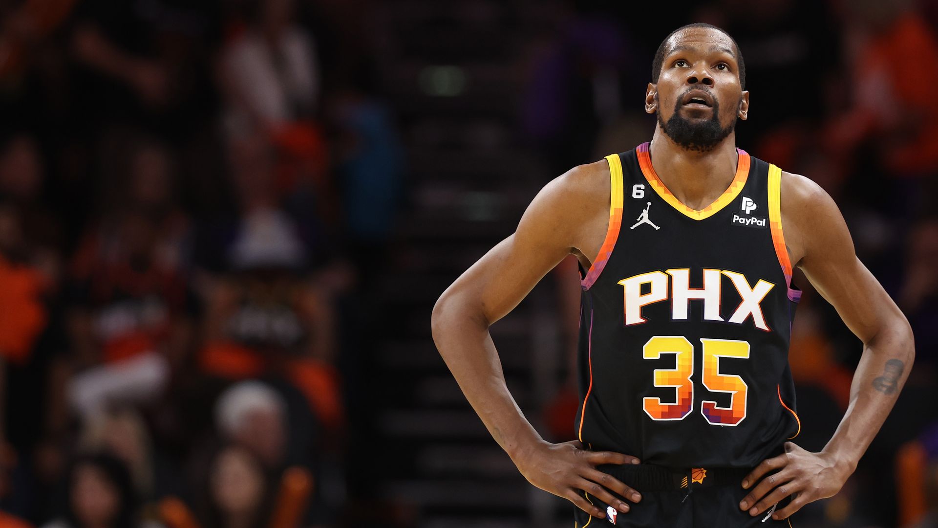 A basketball player looks up while standing with his hands on his hips. 