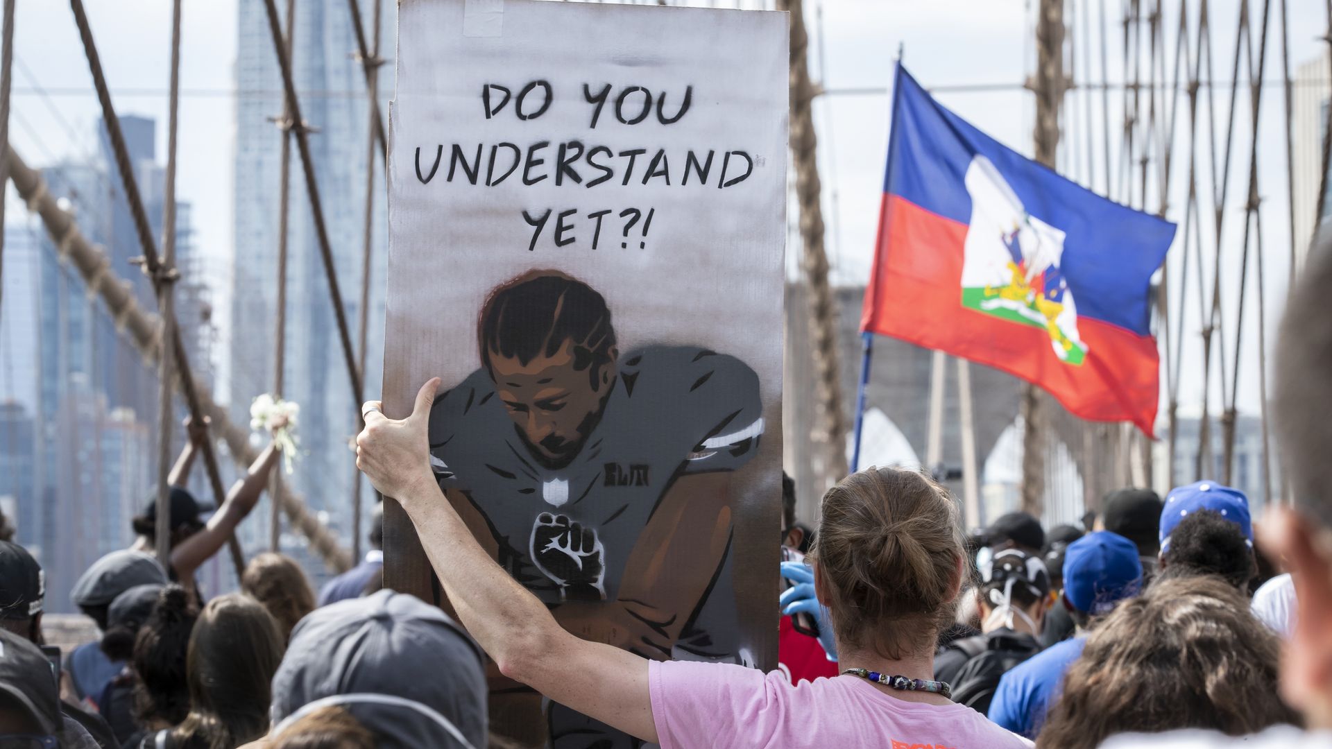 A protester holds a sign with a drawing of Colin who is kneeling and the words: Do you understand yet?