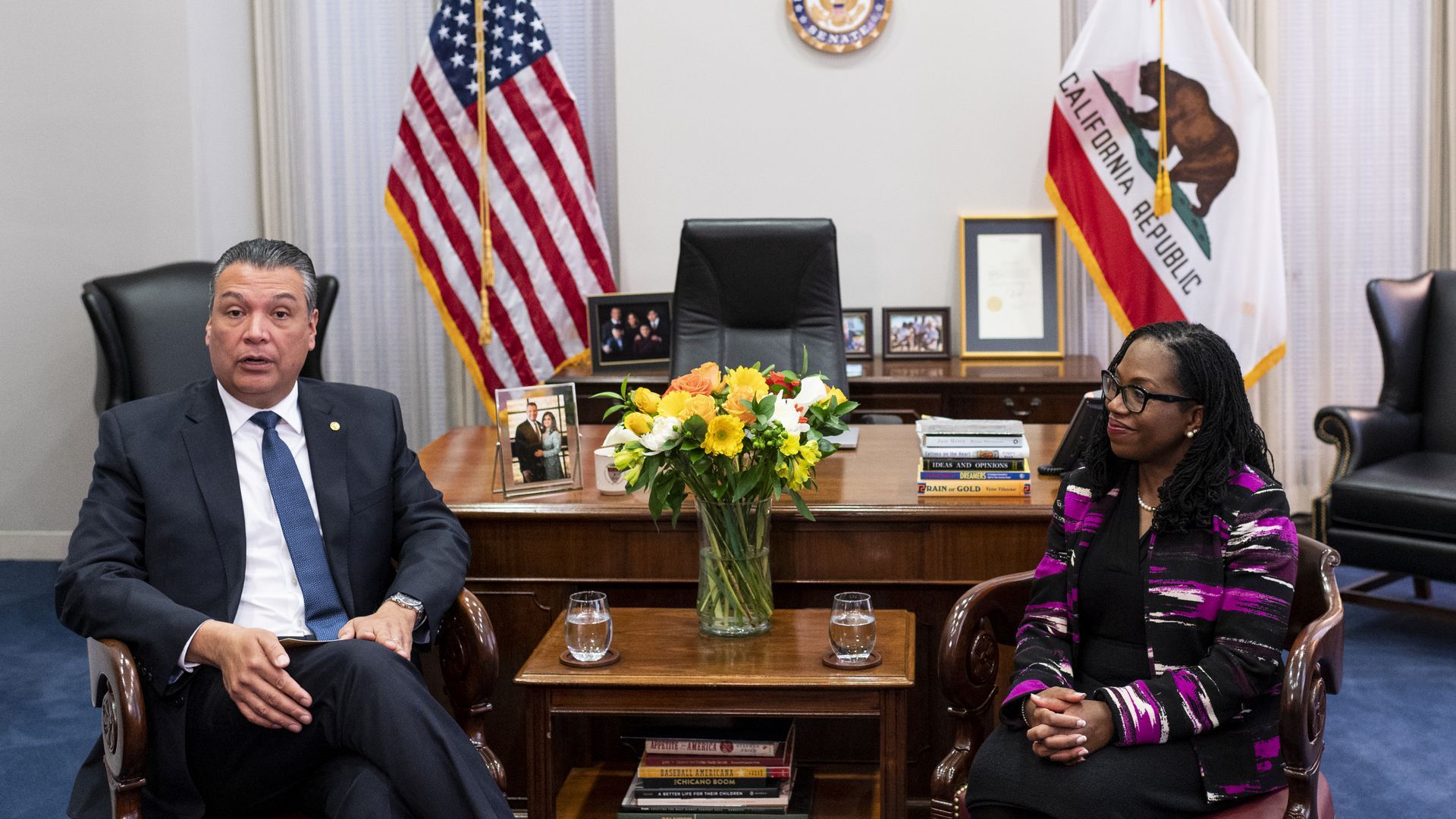 Senator Alex Padilla sits to the left of Supreme Court nominee Ketanji Brown Jackson, who is smiling while looking at him. 