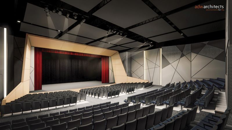 Modern auditorium with a large stage framed by beige panels and red curtains, rows of black seats, dark ceiling with lighting rig, and geometric-patterned gray walls.