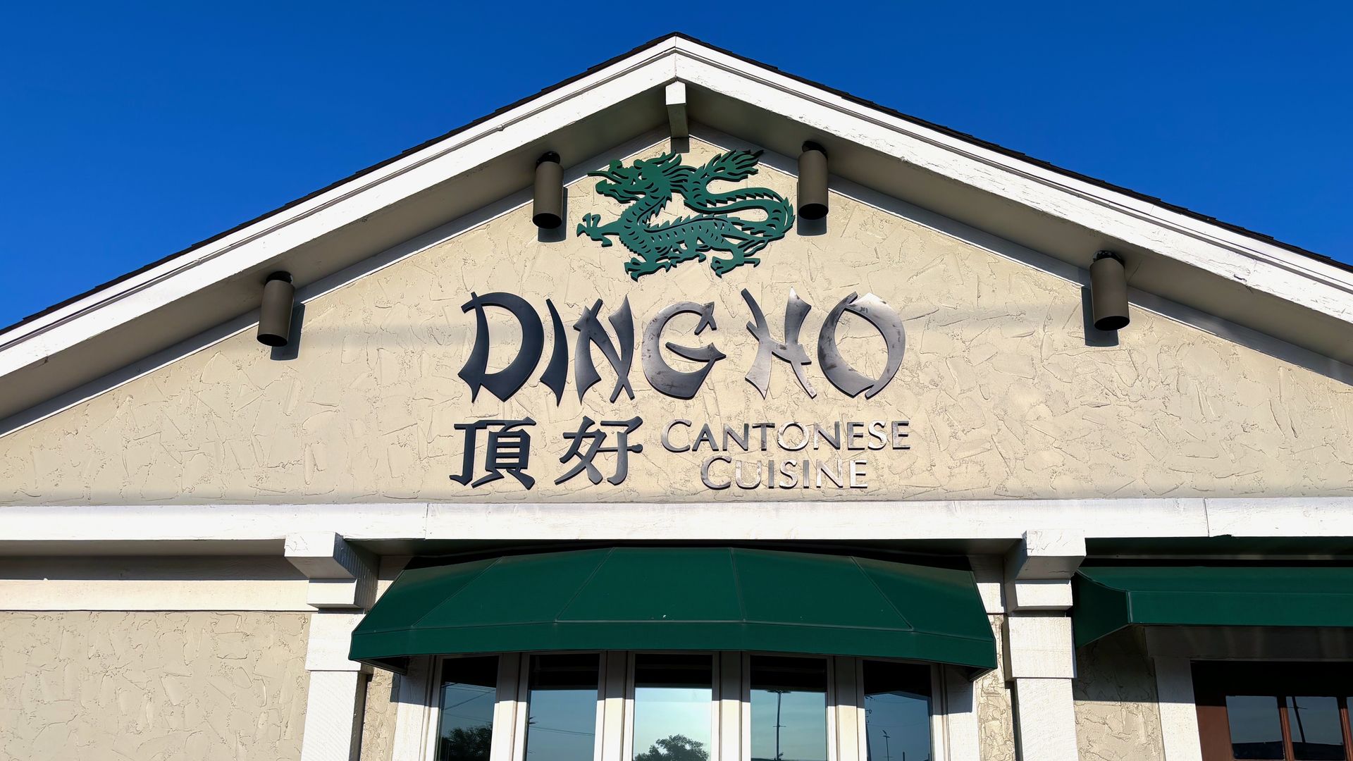 A sign that reads "Ding Ho Cantonese Cuisine" on a building with a green awning and dragon