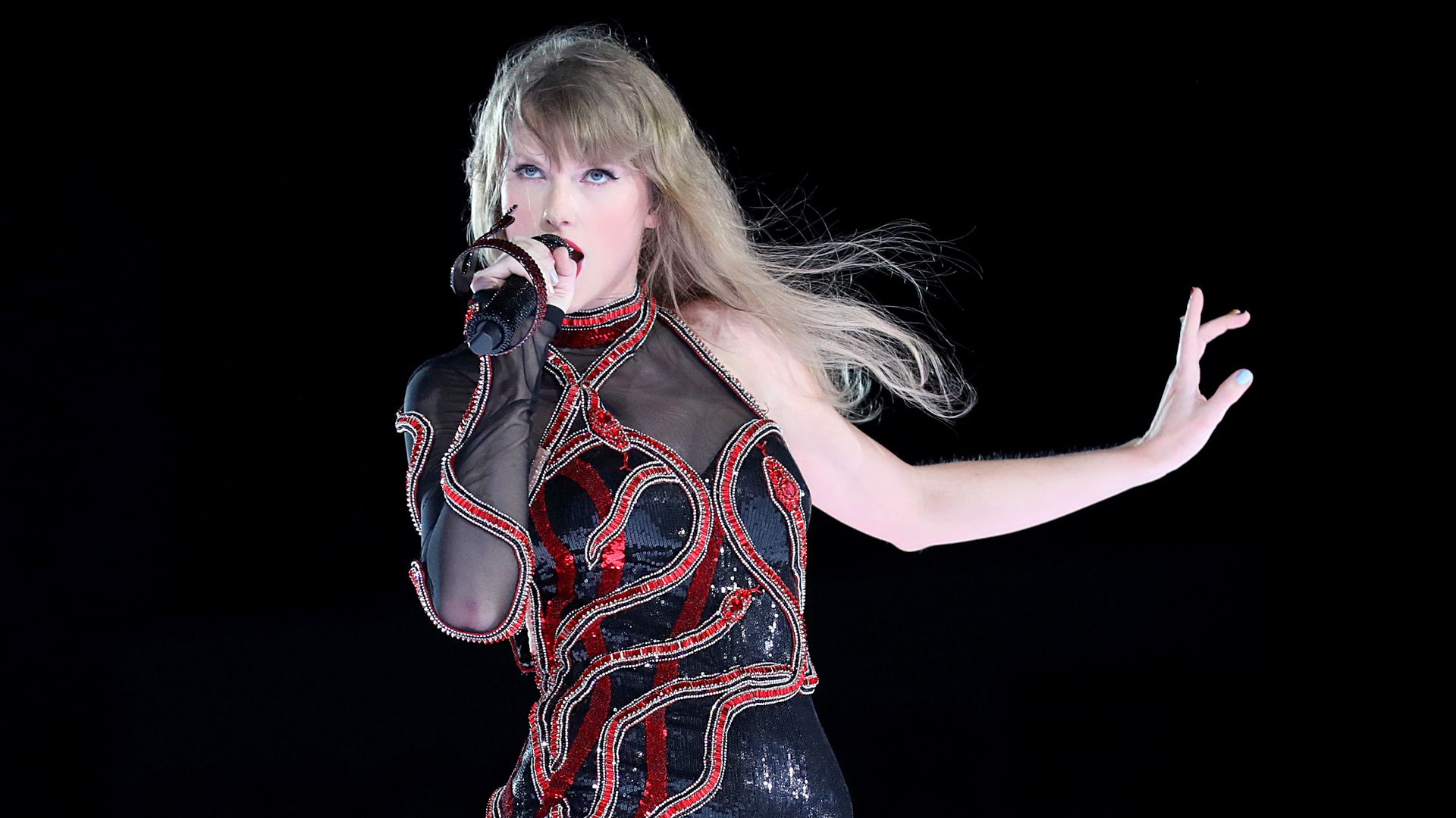 A blond pop star in a sequined black-and-red top singing into a microphone. 