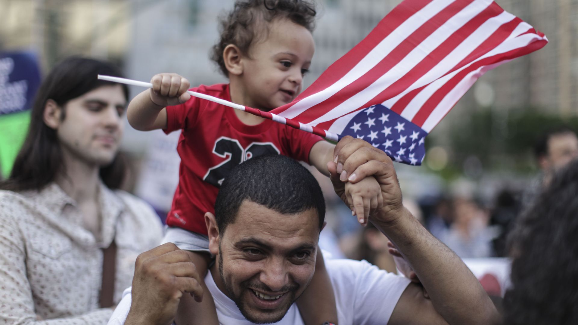 A little boy on his dad's shoulders, waving an American flag.