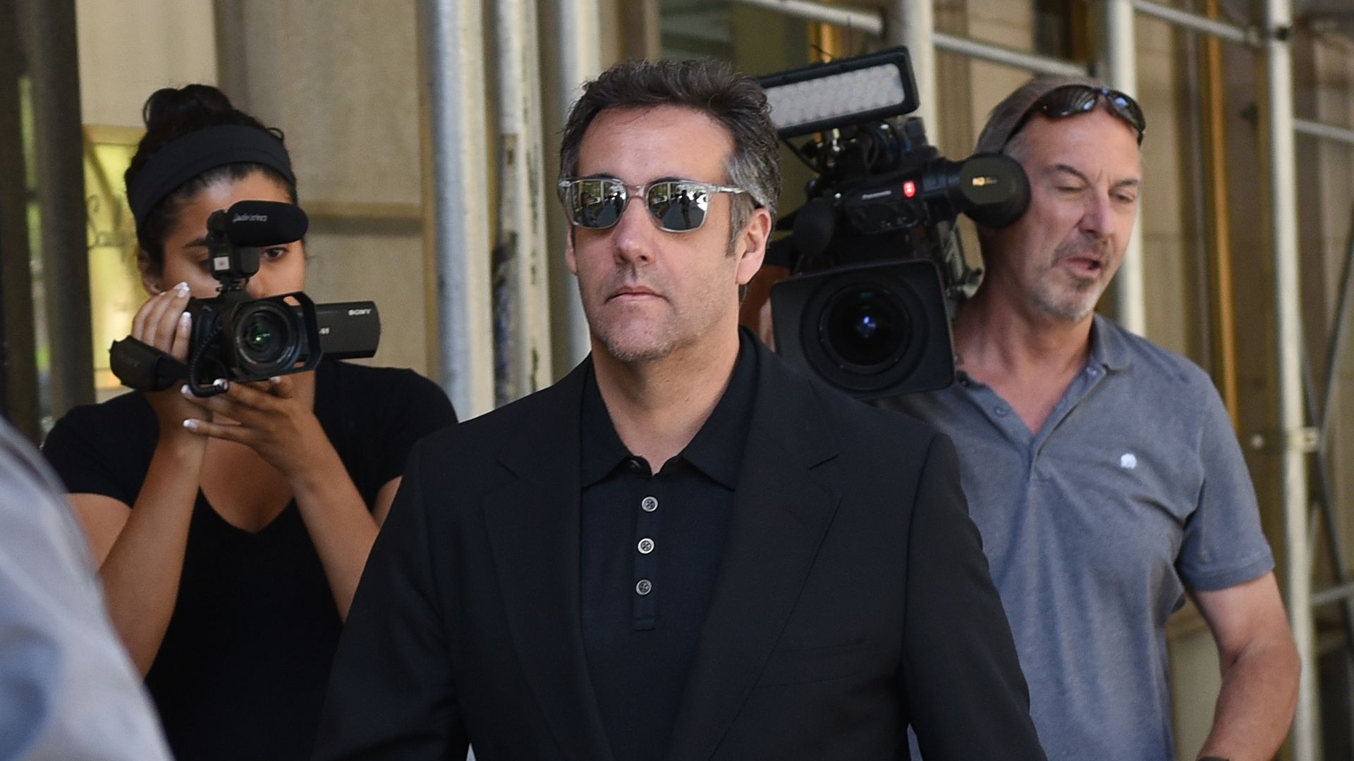 Michael Cohen wearing sunglasses and surrounded by paparazzi 