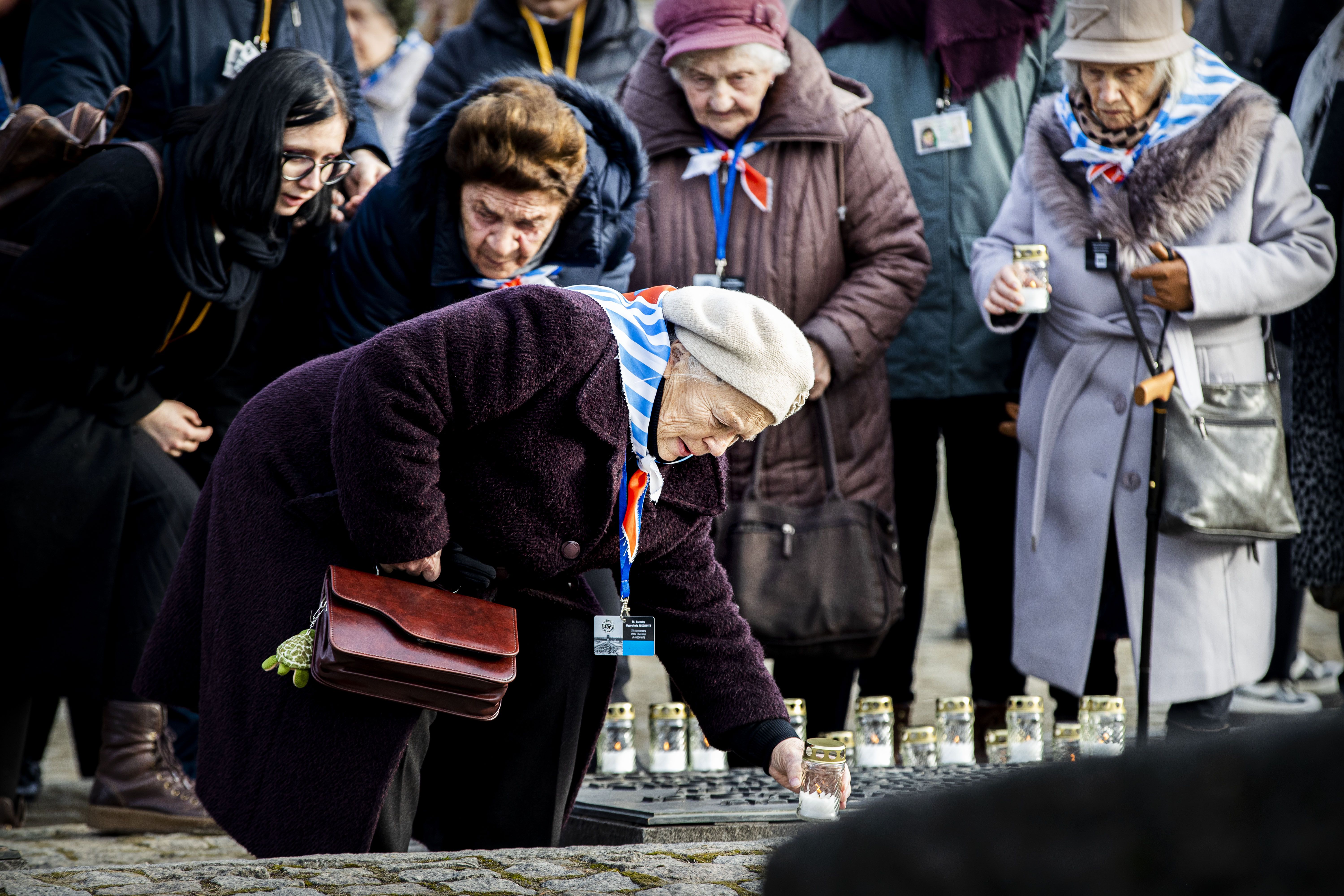 Survivors and family members place candles on a monument 