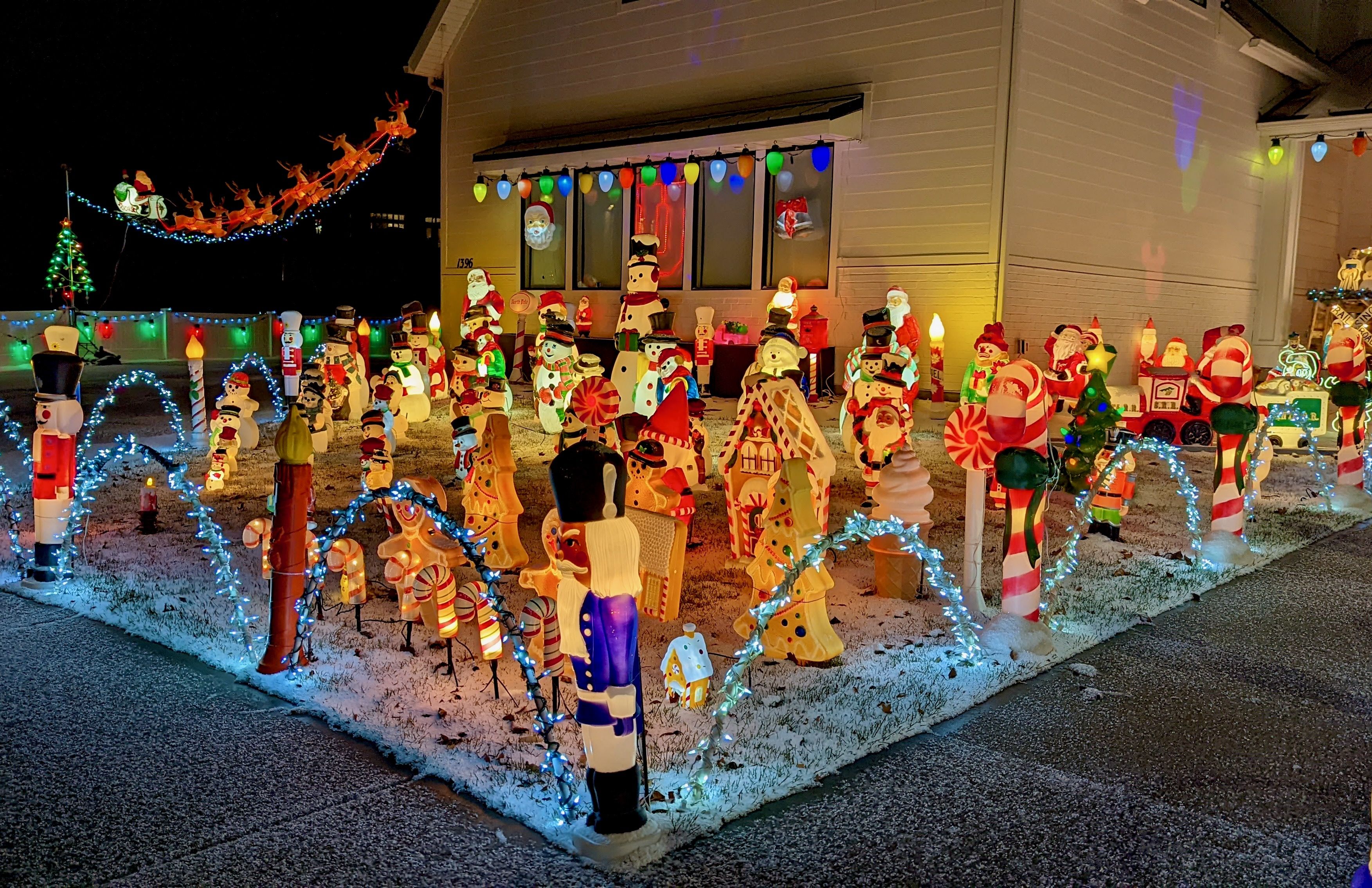 Dozens of Christmas figurines are lighted in a lawn, with a light-up Santa and reindeer ascending toward the roof. 