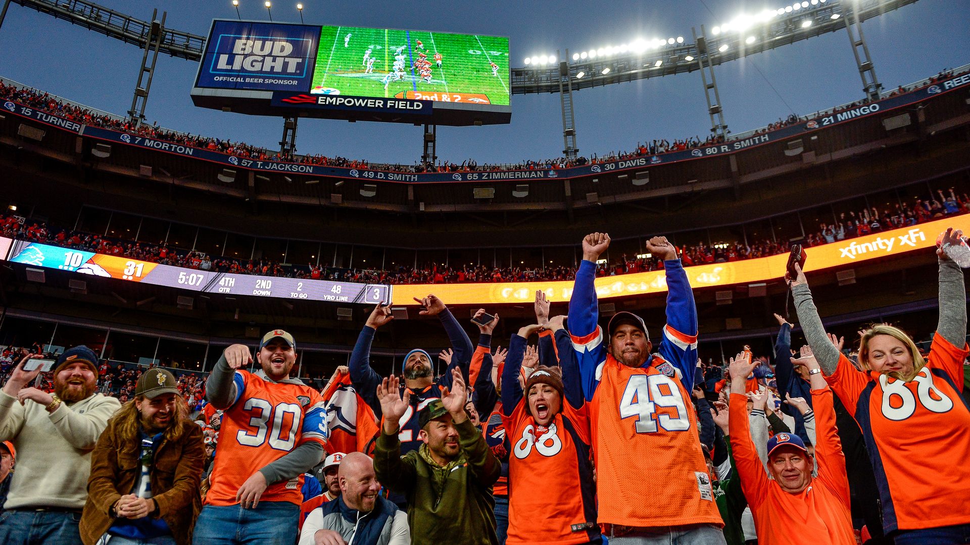 Several Broncos fans cheer during a nighttime game at Empower Field in Denver. 