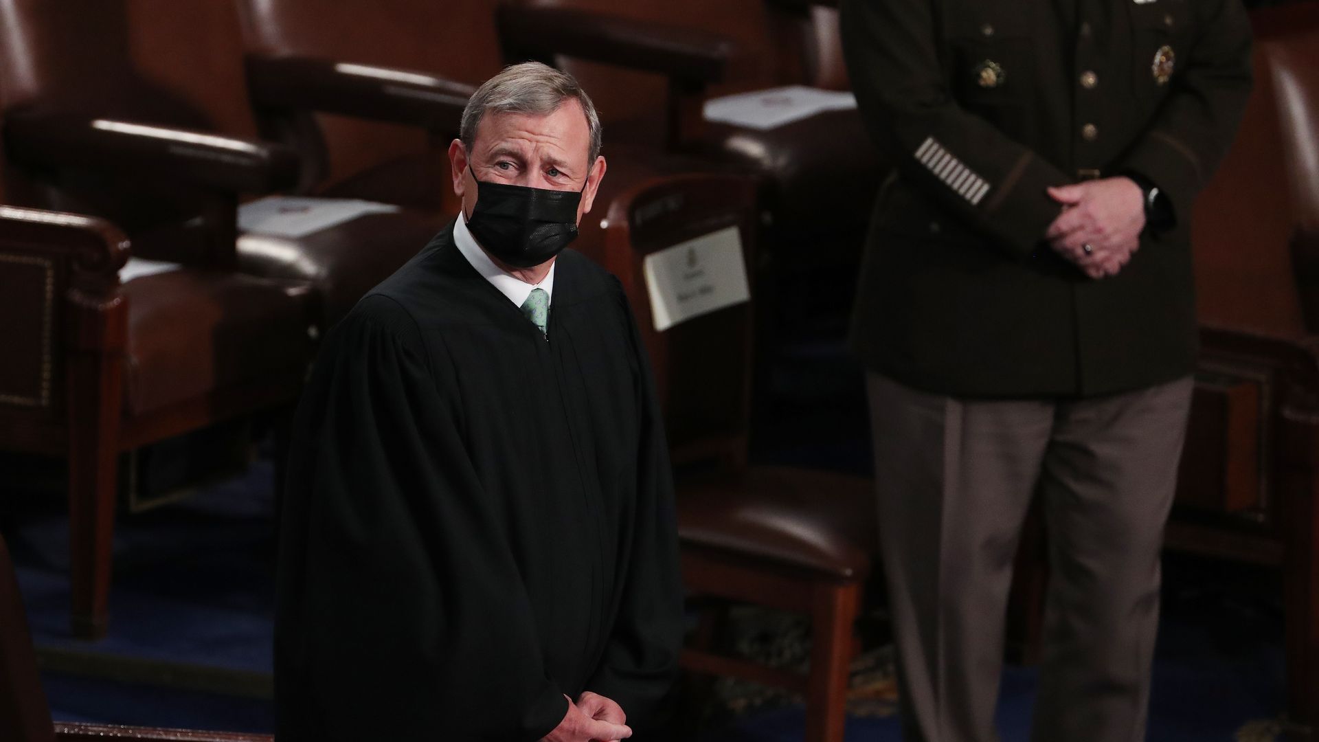 Photo of John Roberts in a mask and his Supreme Court robes while standing in a chamber with hands clasped