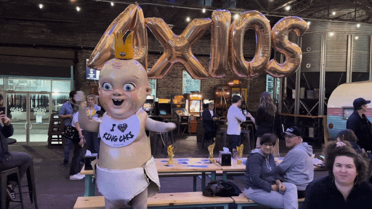 A gif of King Cake Baby dancing in front of balloons that spell AXIOS.