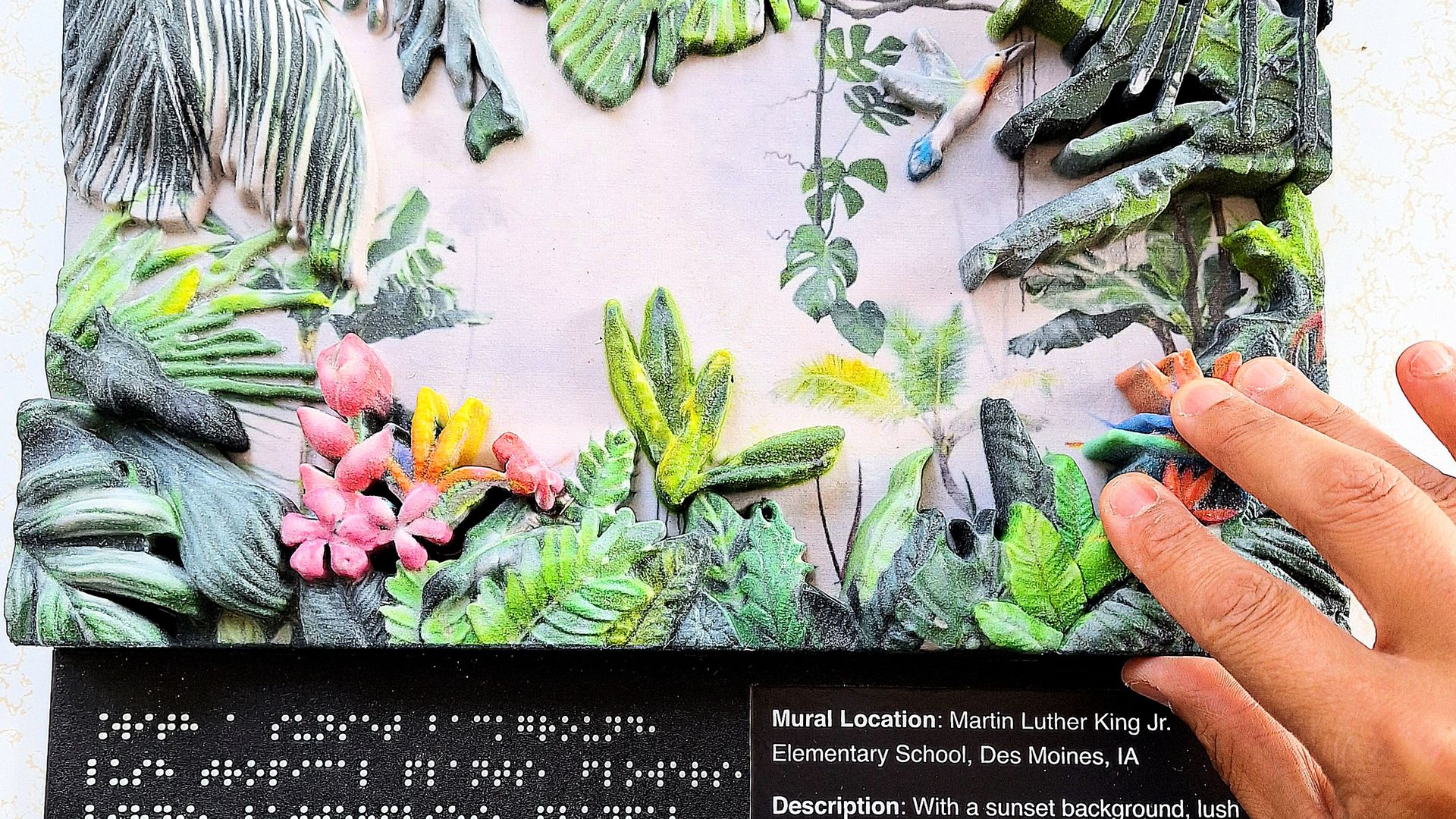 A 3D printed mural with a hand over it showing braille