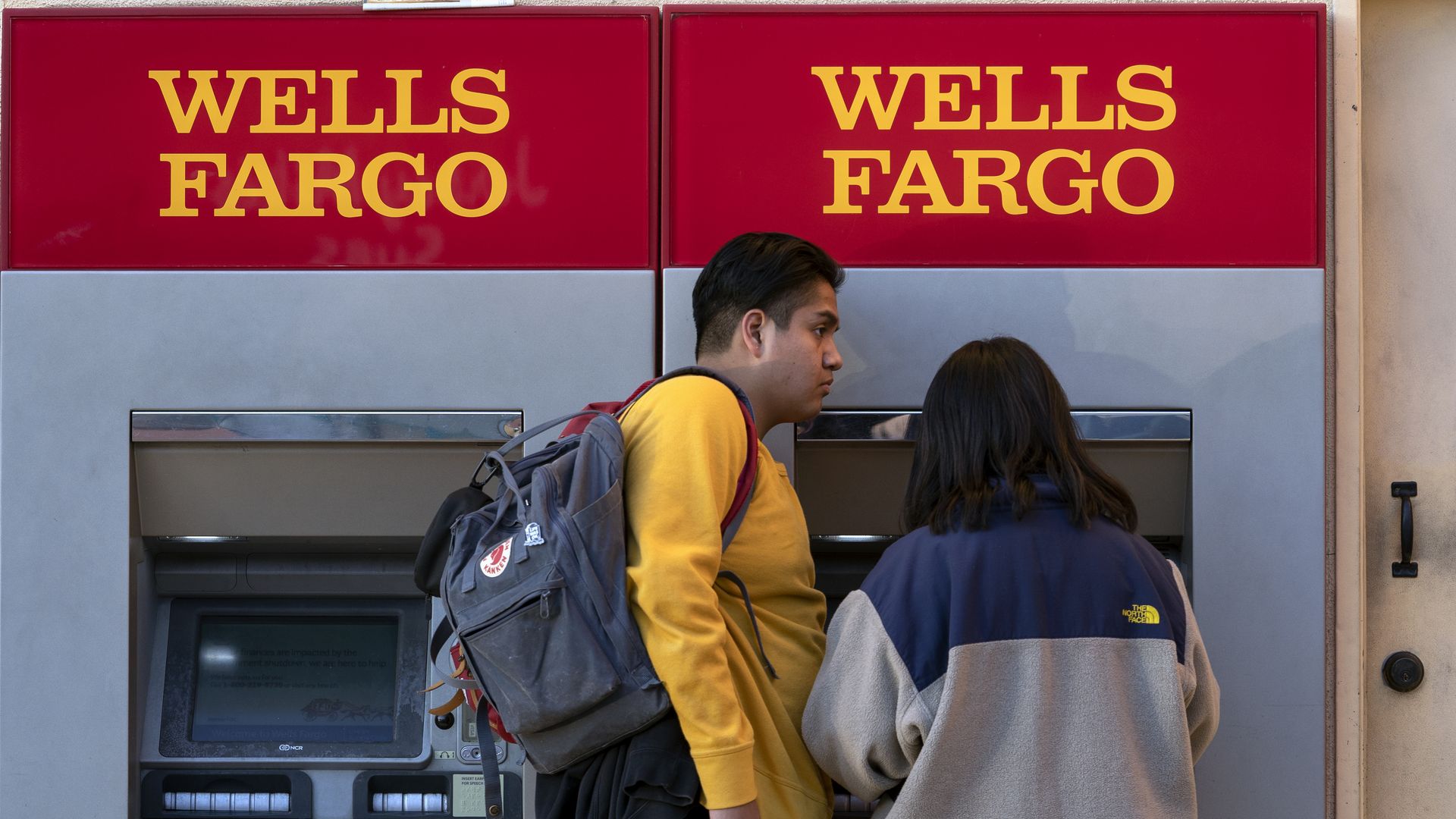 In this image, two people stand in front of a Wells Fargo ATM 