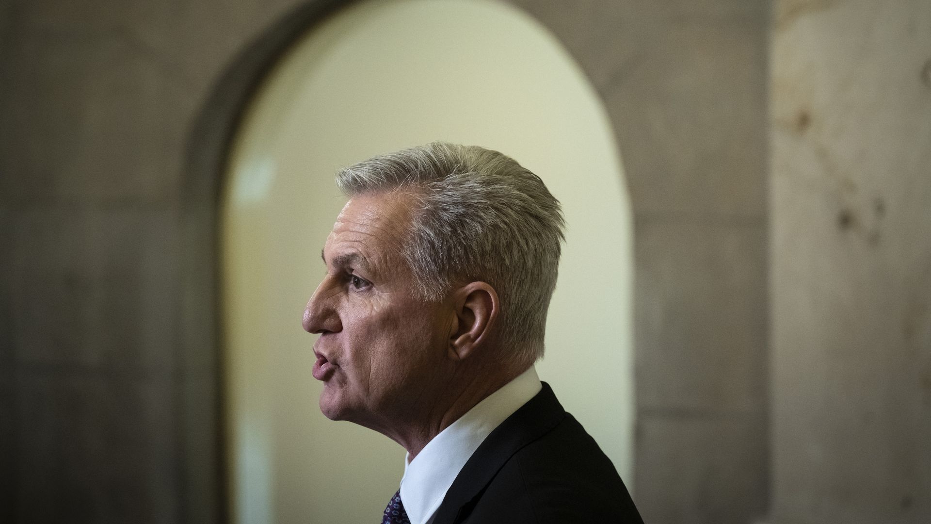 House Speaker Kevin McCarthy, wearing a dark gray suit, white shirt and purple tie, speaks to reporters in front of his Capitol office.