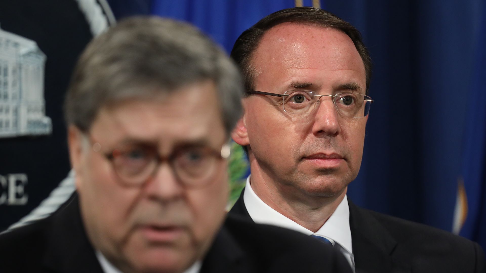 In this image, Rod stands behind Bill Barr in sharp focus while Barr is slightly blurred and unfocused through the camera lens.