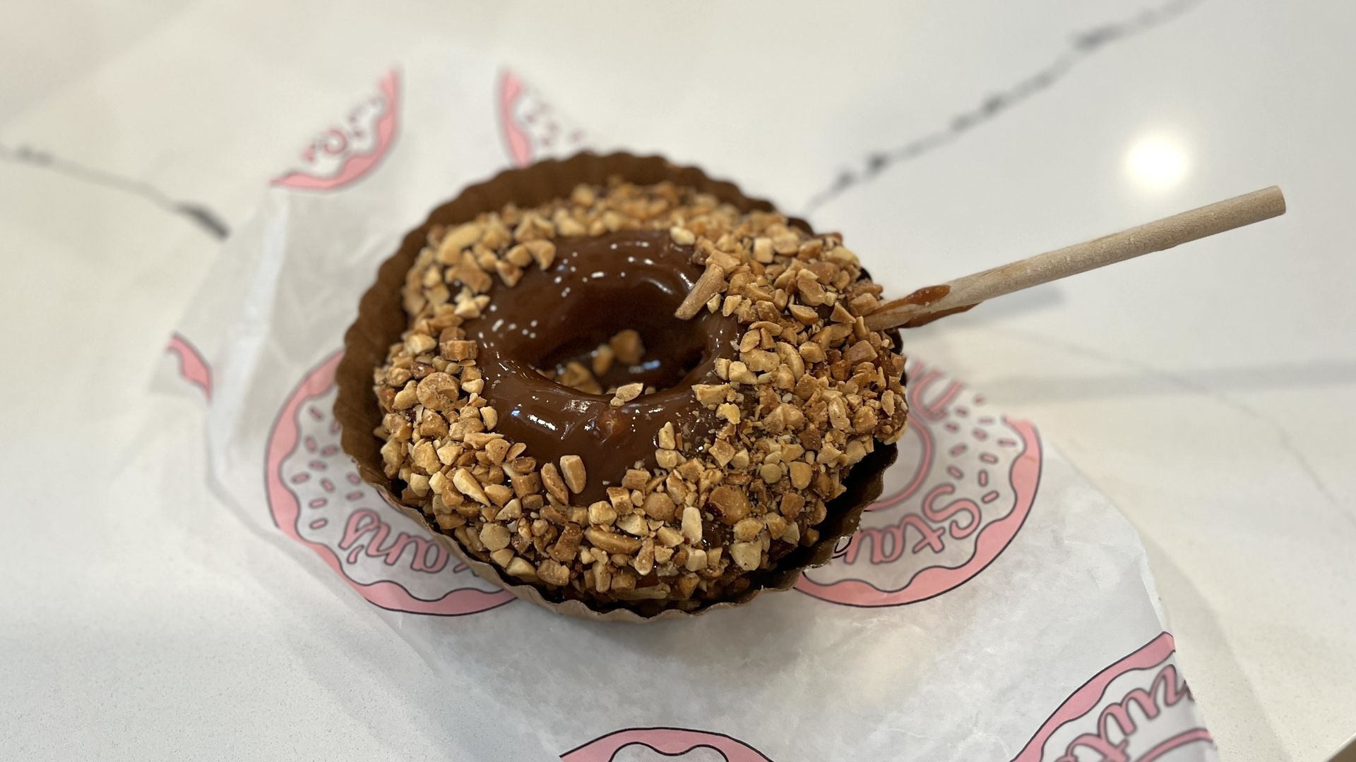 A doughnut on a wooden stick covered in caramel and peanuts 