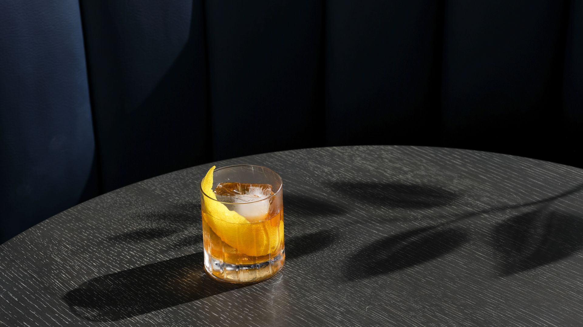 A golden-hued cocktail sits on a sparse table. 