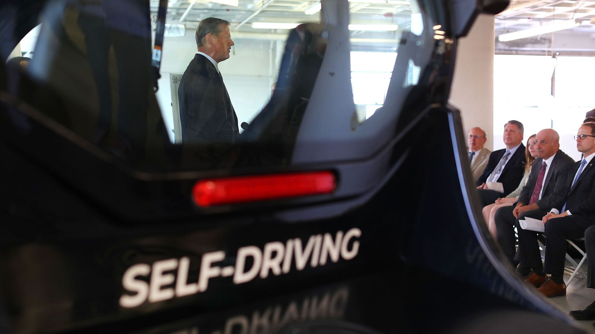 In this image, the words "self-driving" are seen on the back of a black car. 