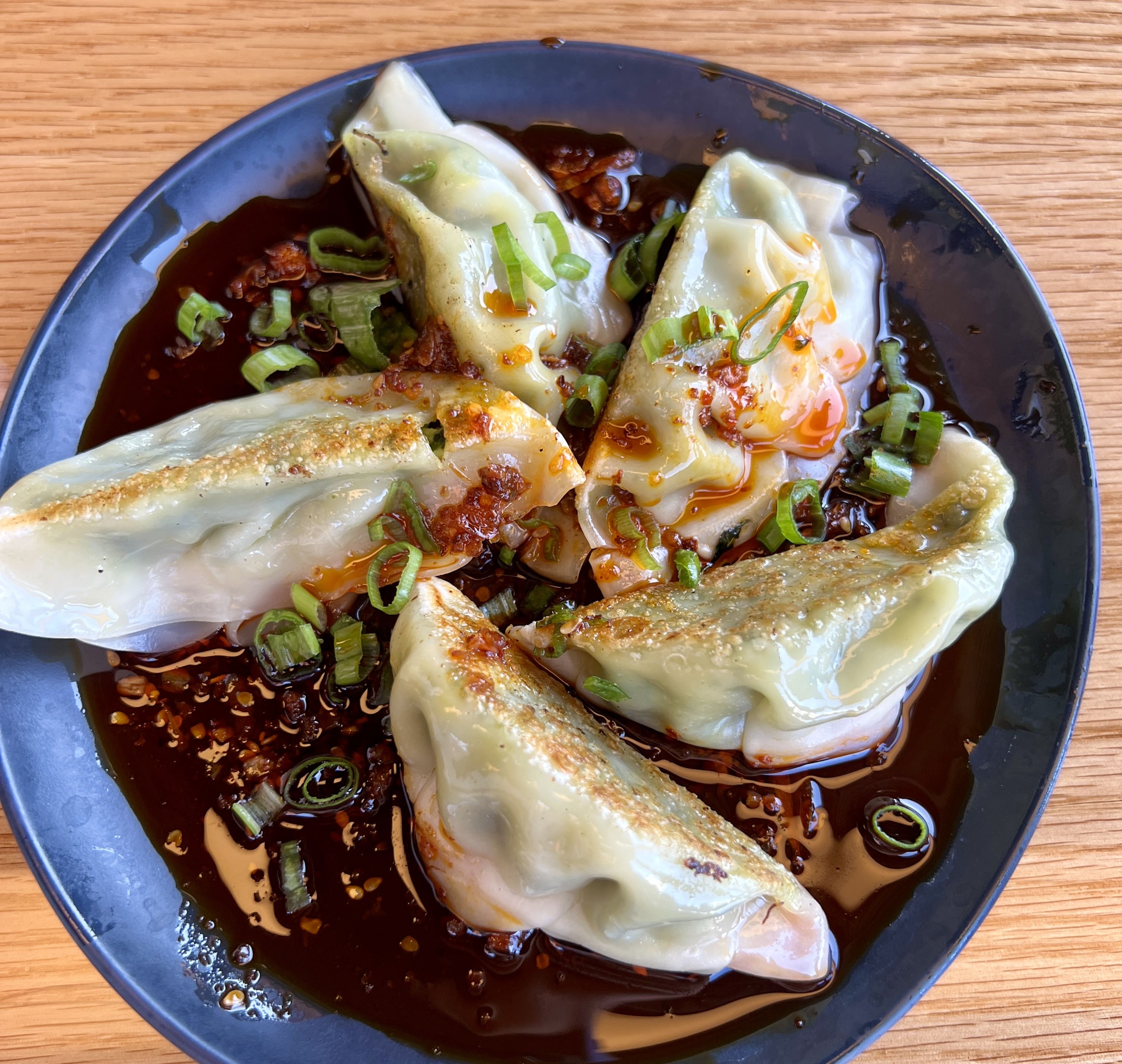 vegetable gyoza sits in oil on a blue plate