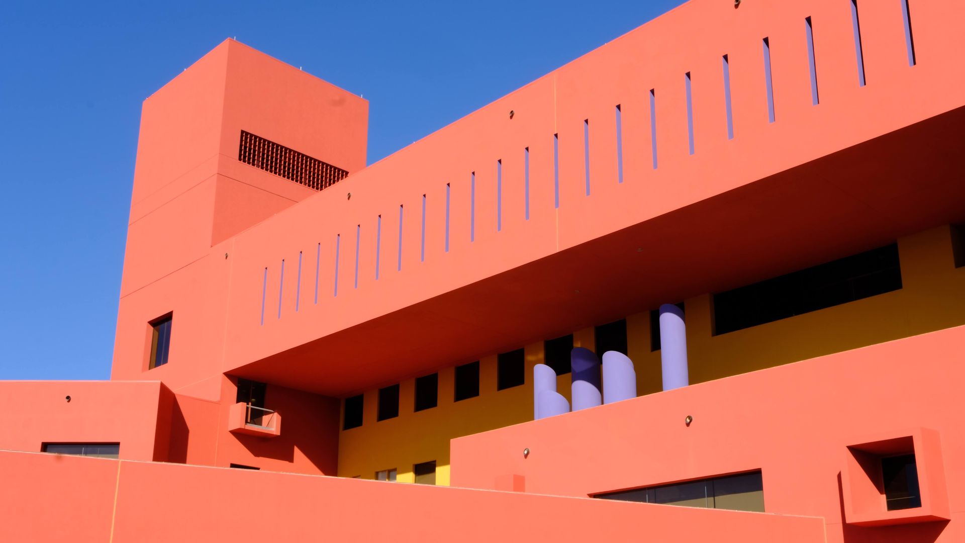 A bright red Central Library building is seen against a clear blue sky.