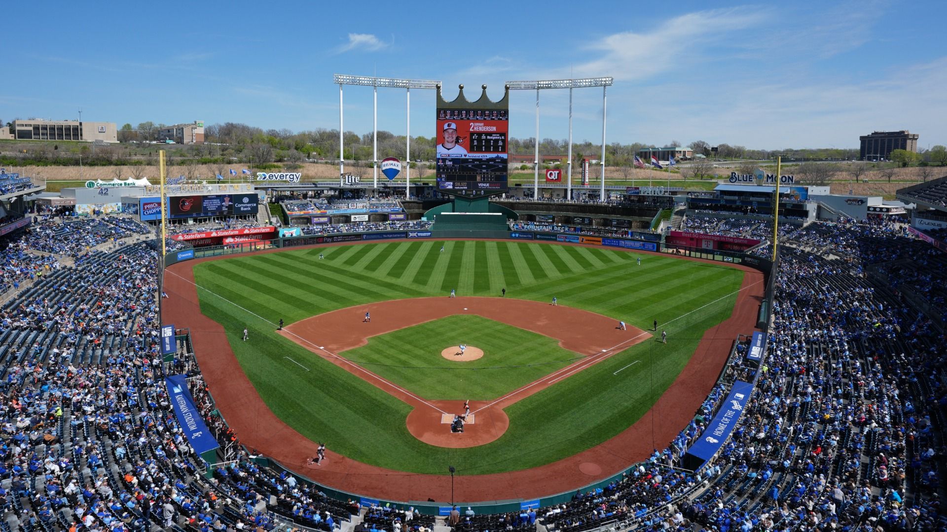 Photo of the infield at Kauffman Stadium looking out toward the Crown Vision board with fans in the stands on a partly cloudy day.