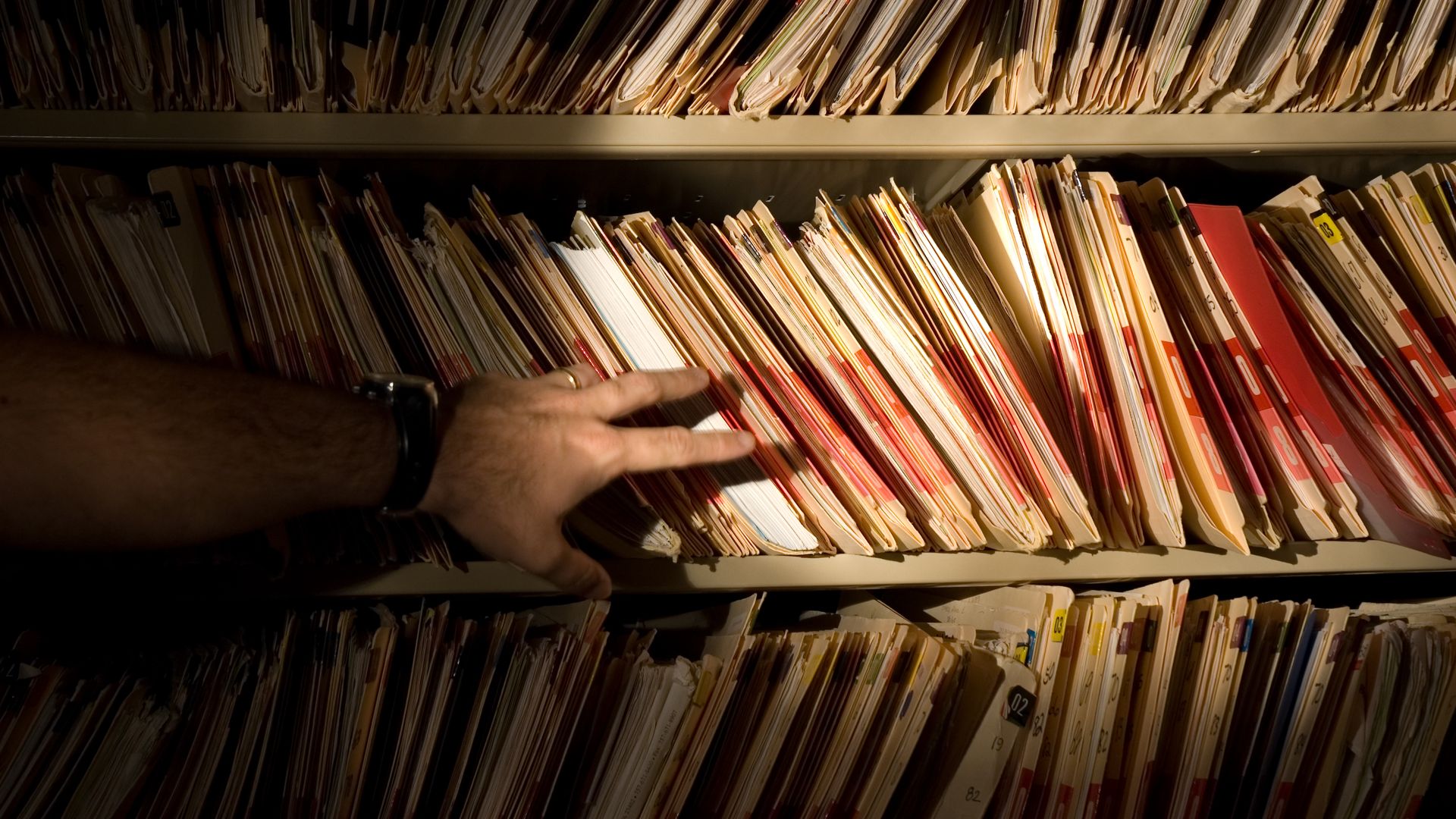 Photo of a hand reaching out to pull paper file folders from a shelf