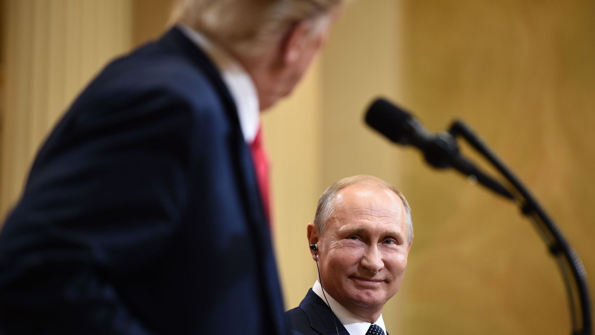 Vladimir Putin smiles at Trump, who looks at him over his podium.