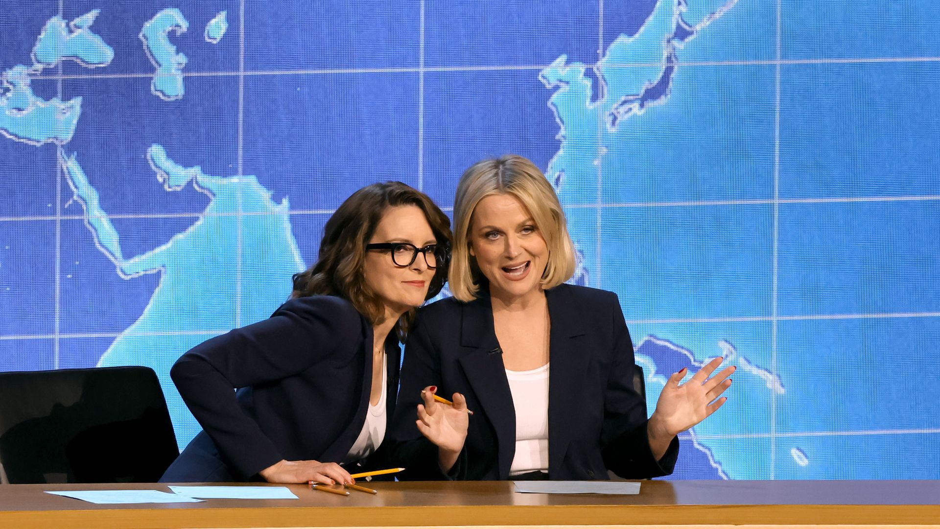 two women at a news desk in front of a map 