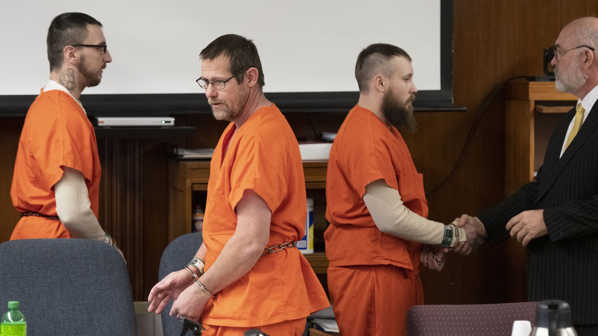 the three prisoners in handcuffs and wearing orange jumpsuits in court