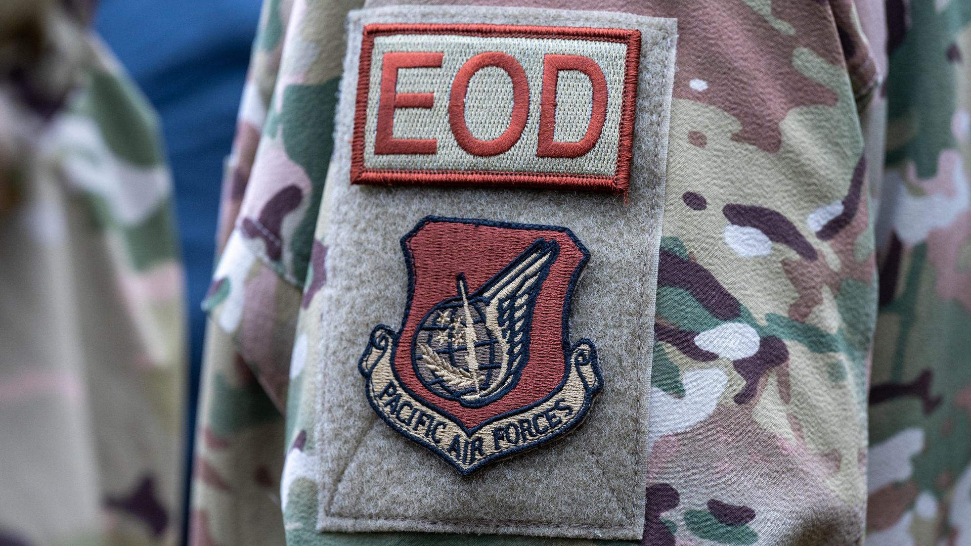 Military uniform sleeve with camouflage pattern showing a patch labeled "EOD" above a "Pacific Air Forces" emblem featuring a winged globe and sword.
