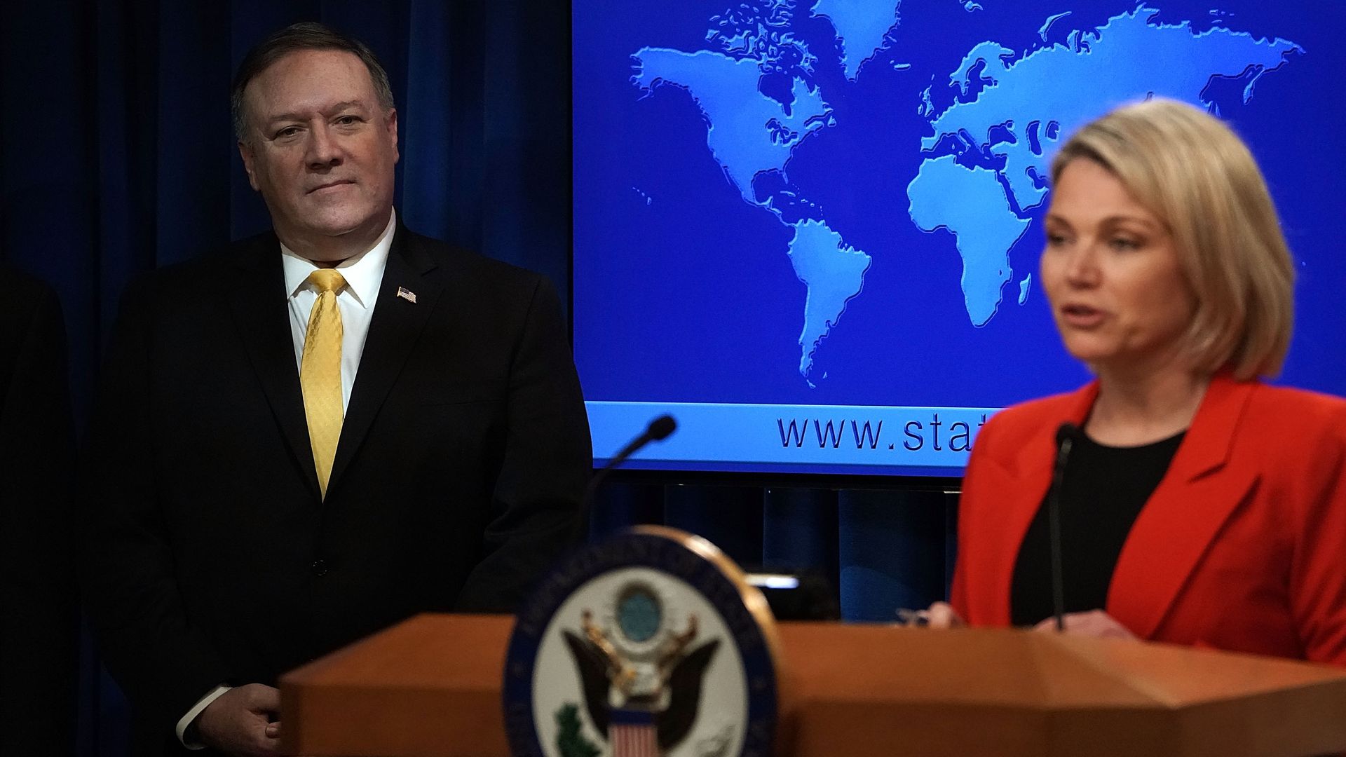 State Dept spokeswoman Heather Nauert speaks at a podium while Mike Pompeo watches from behind