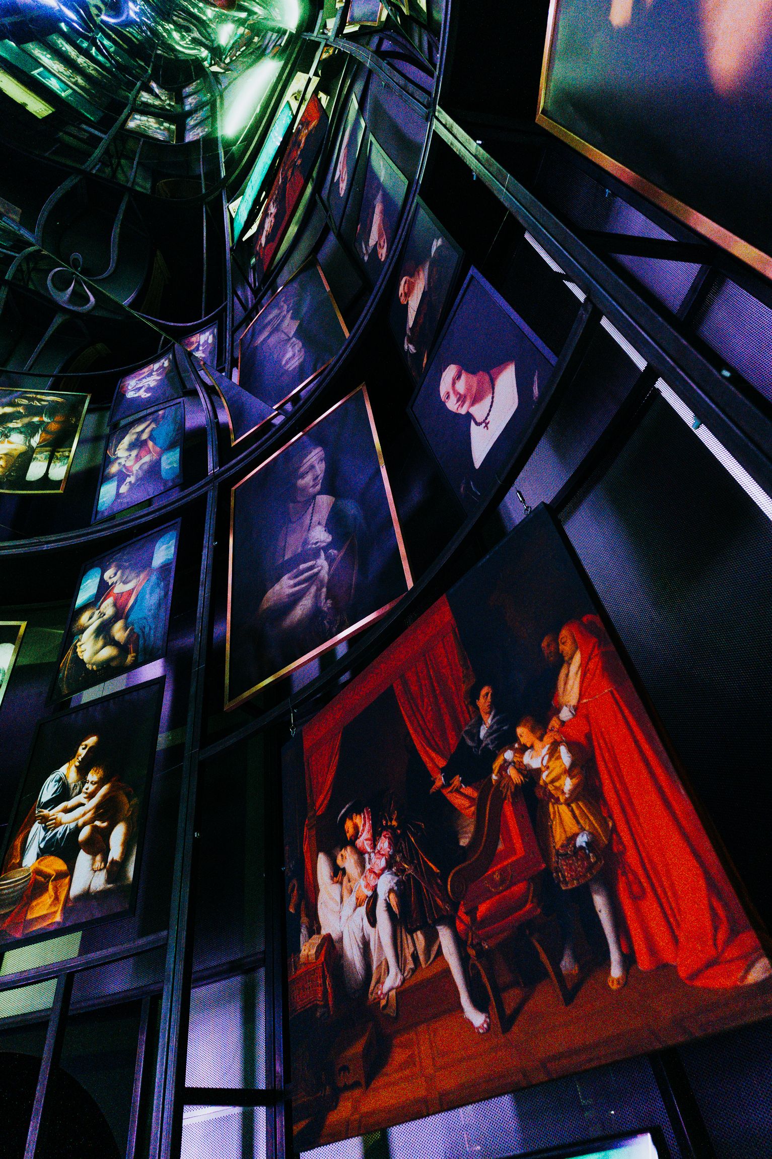 Curved gallery wall filled with hanging framed paintings and portraits in blue and purple lighting, with a green neon glow at the top left and a red-draped painting near the bottom right.