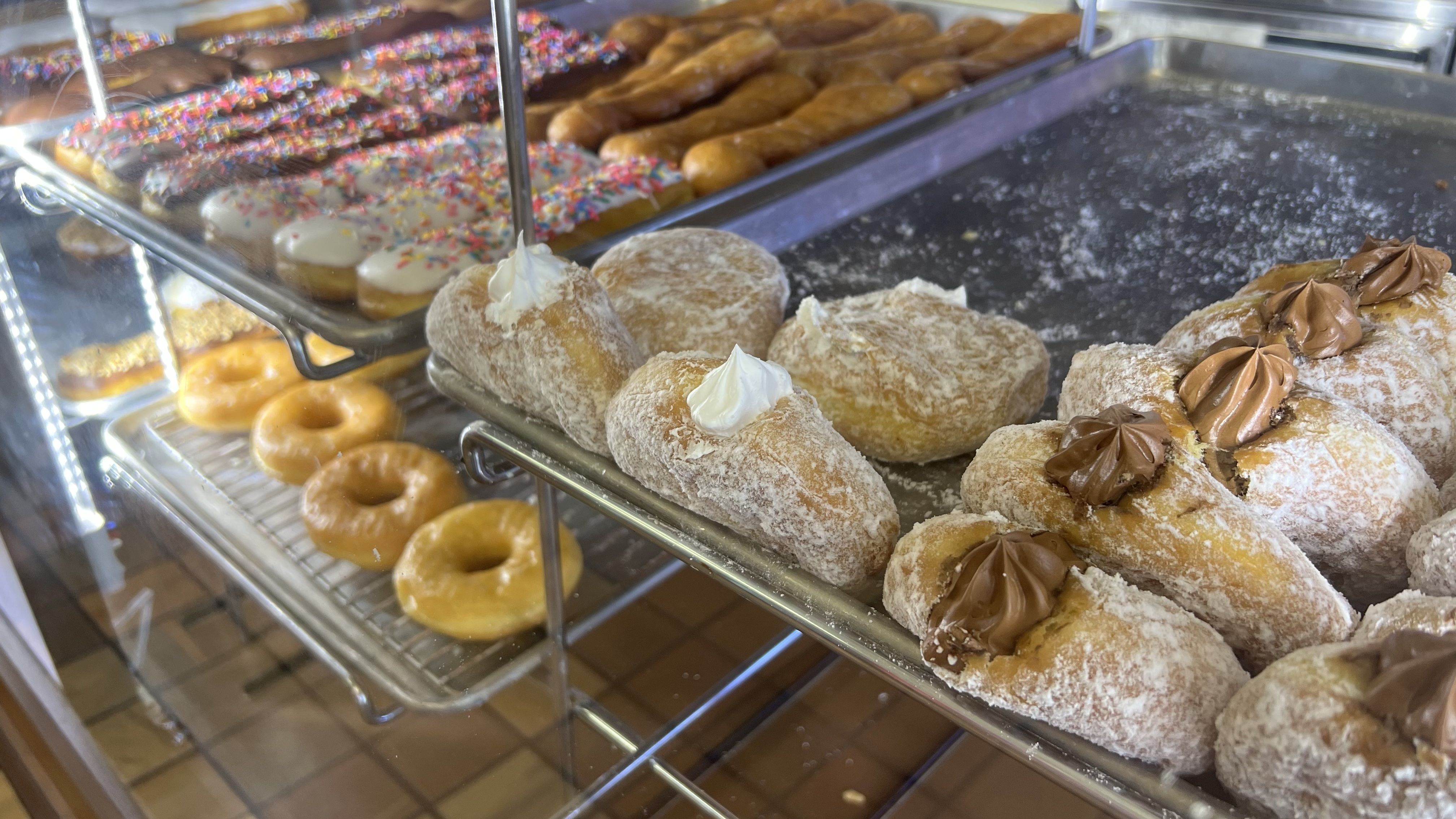 Filled Bismarck donuts in a display case at a bakery with vanilla and chocolate frosting