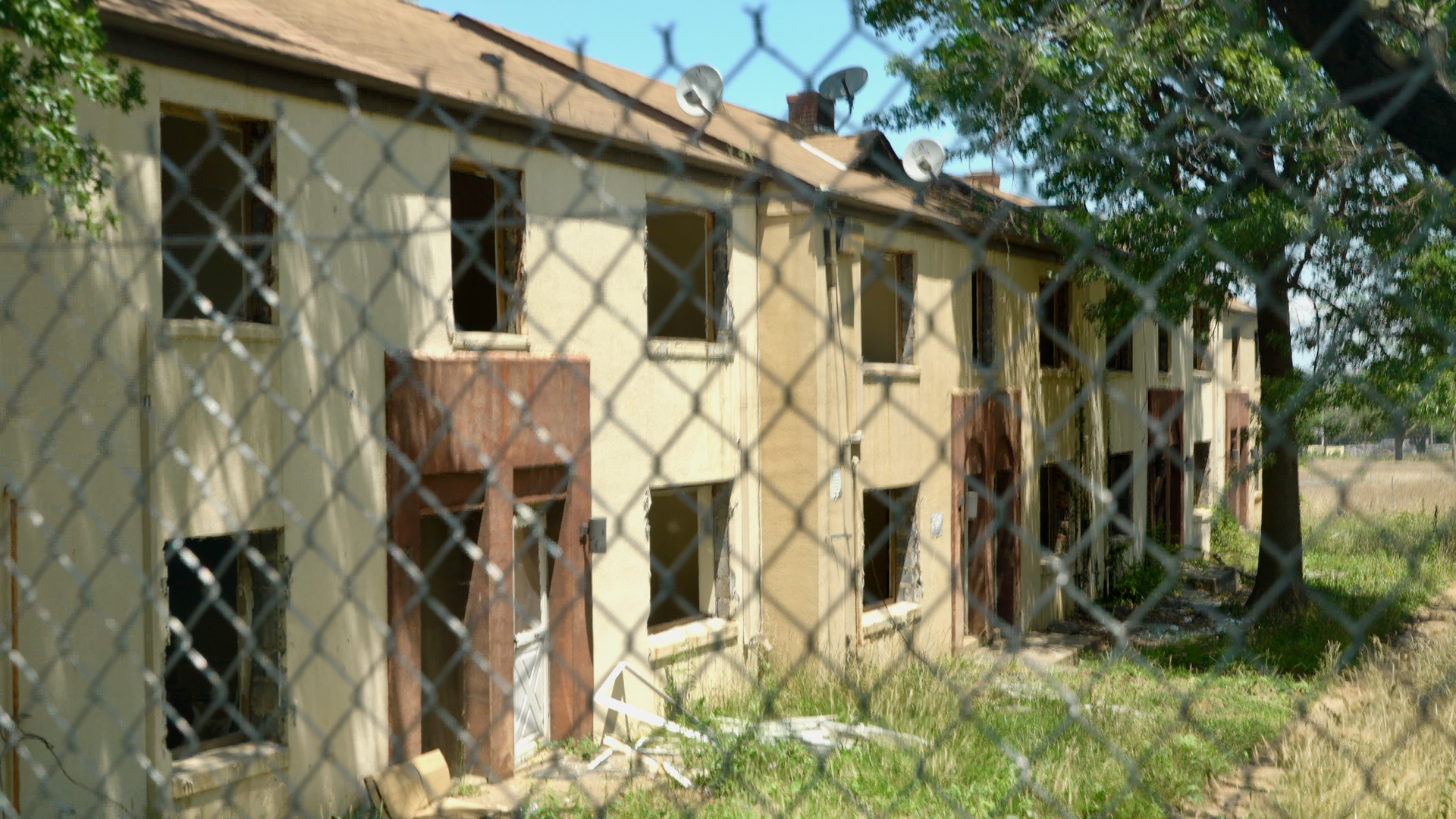 A row of tan houses sit behind a fence in the foreground.