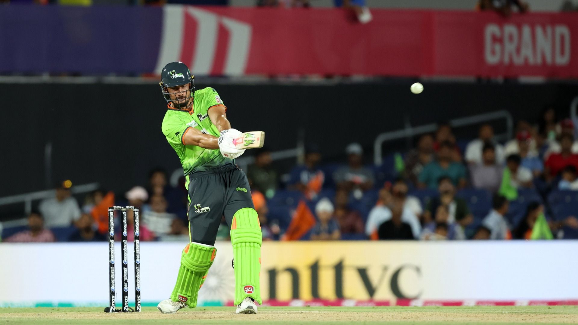 A cricket player in bold lime swings the bat.