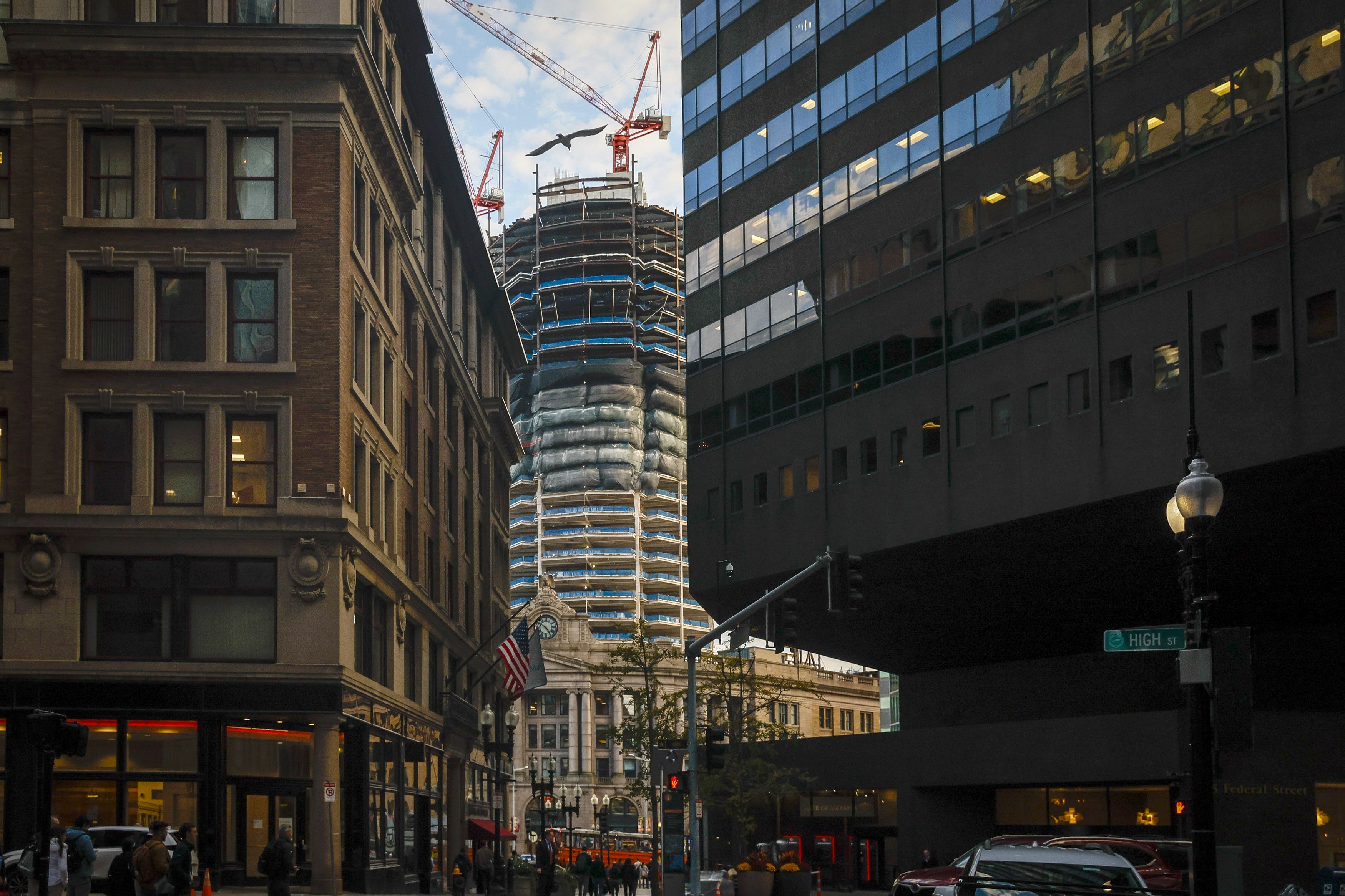 Behind two buildings in downtown Boston is the construction site of the South Station Tower, with two cranes placed at the top of the 51-story tower.