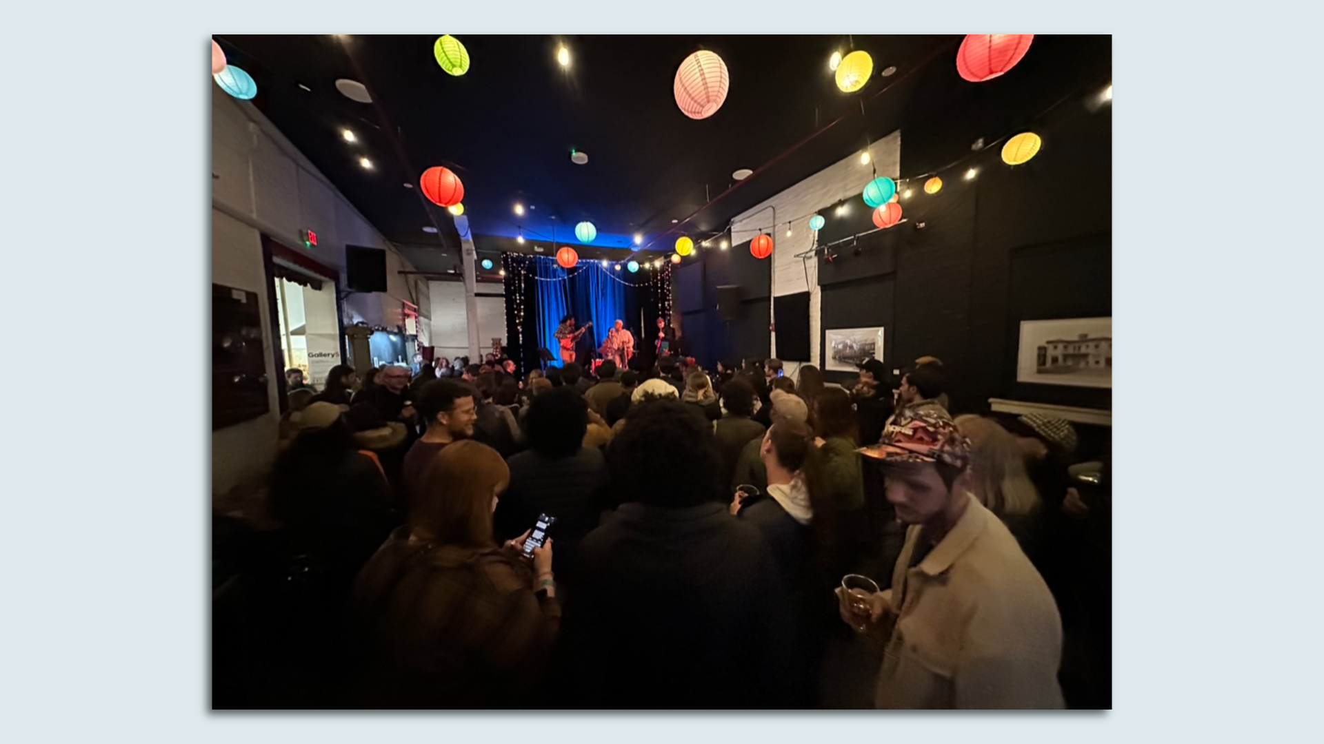 a crowd of people stand inside an art gallery with a stage 