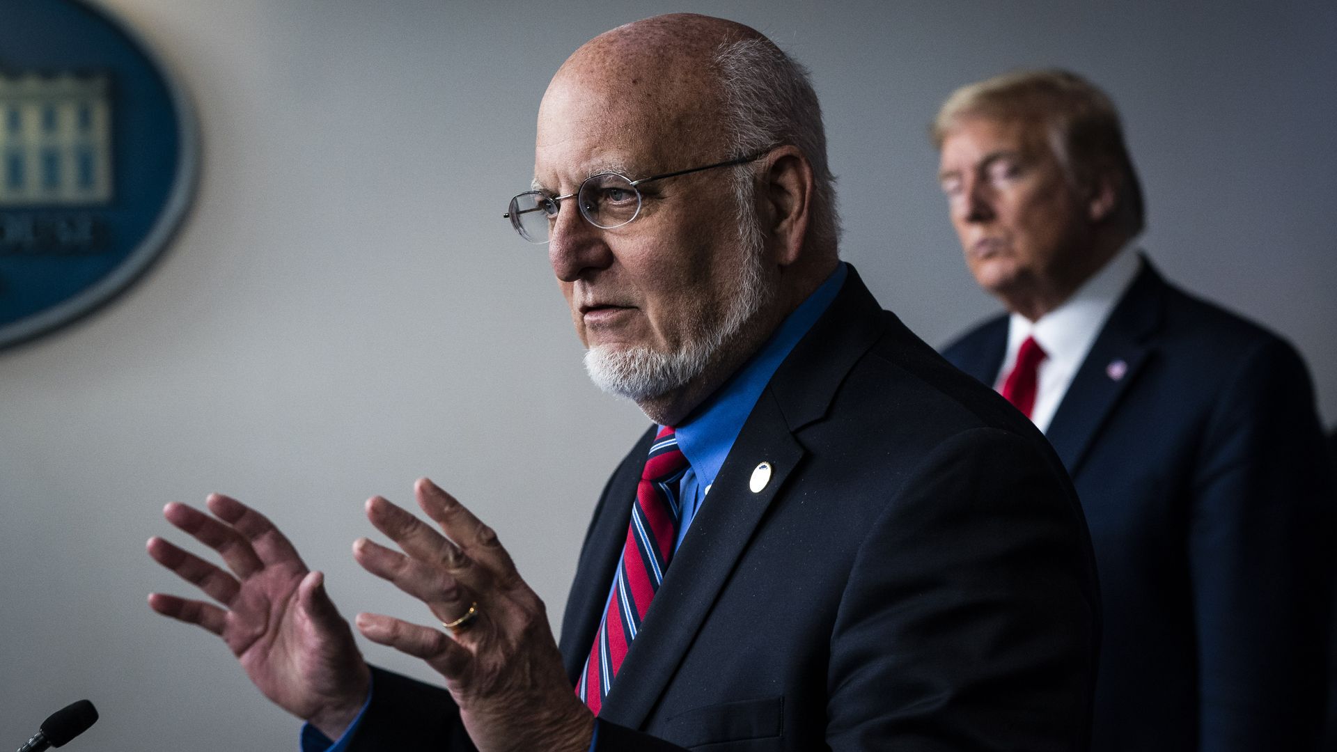 In this image, Trump stands behind CDC director Robert Redfield