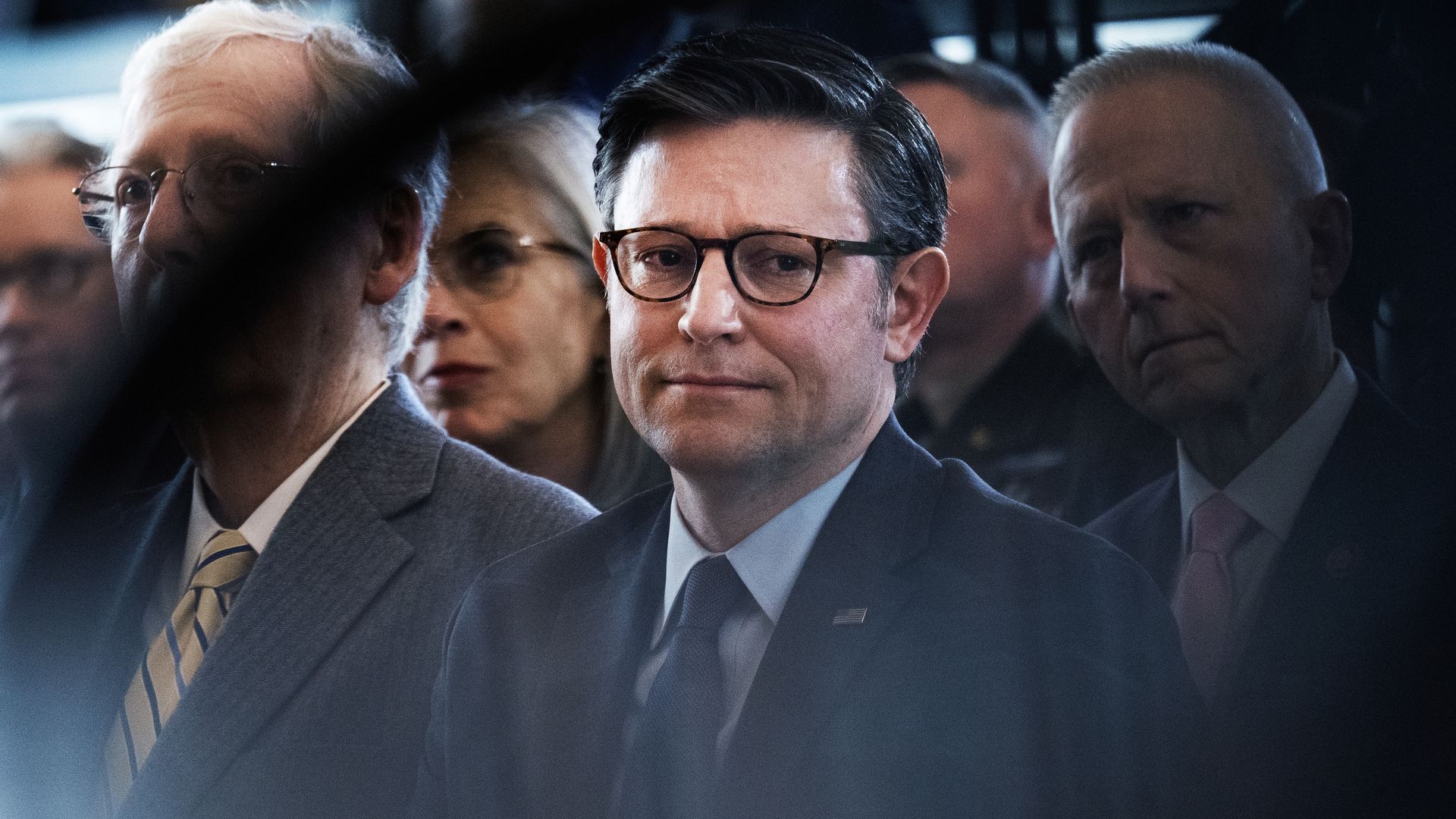Mike Johnson, wearing a dark blue suit, white shirt, blue tie and glasses, flanked by fellow members of Congress.