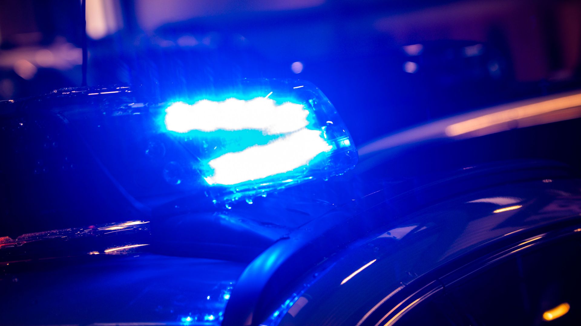 Close-up of bright blue flashing police lights on top of a dark vehicle at night, with reflections and blurred background.