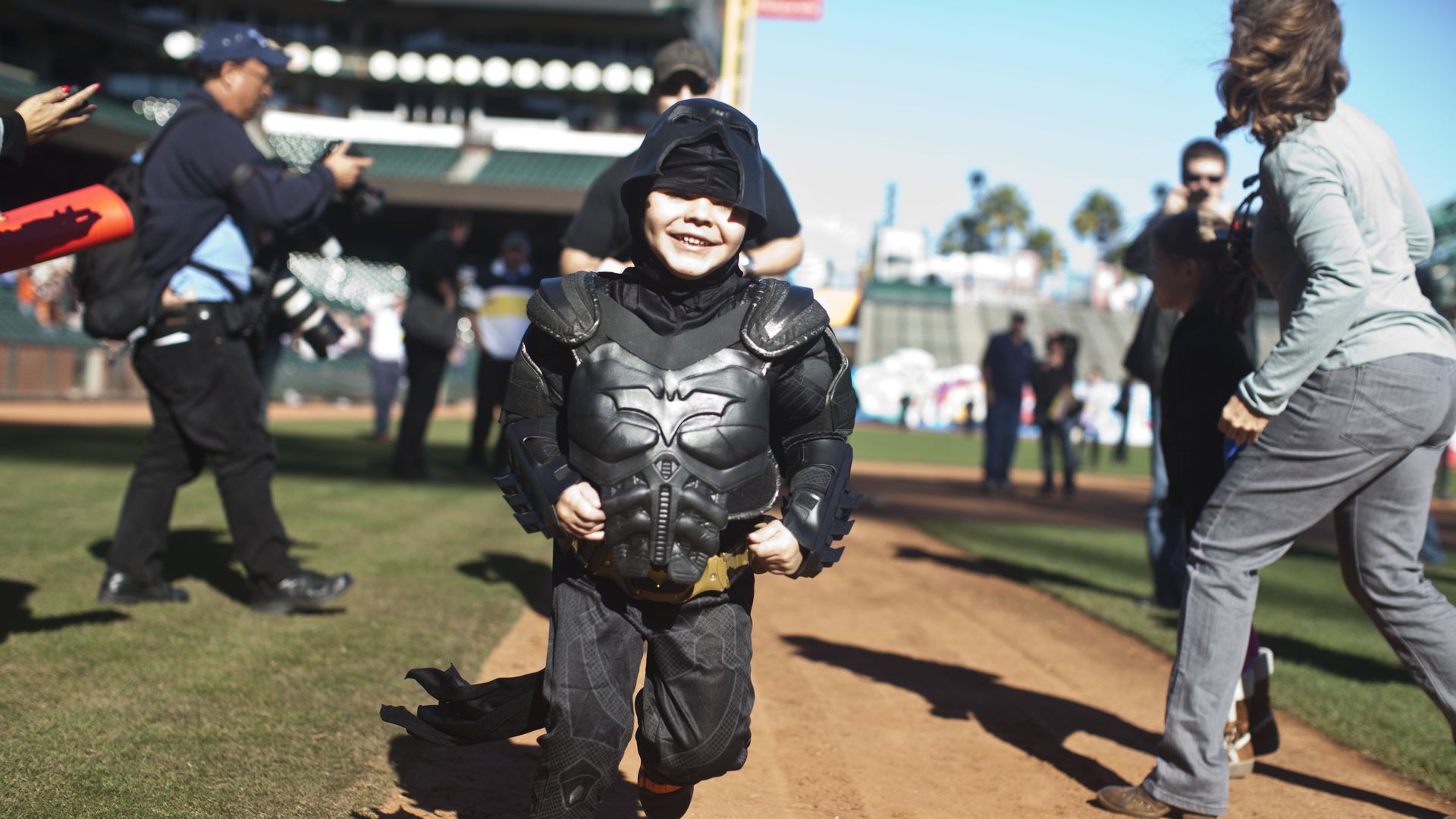 Photo of a young boy dressed as Batkid smiling as he runs