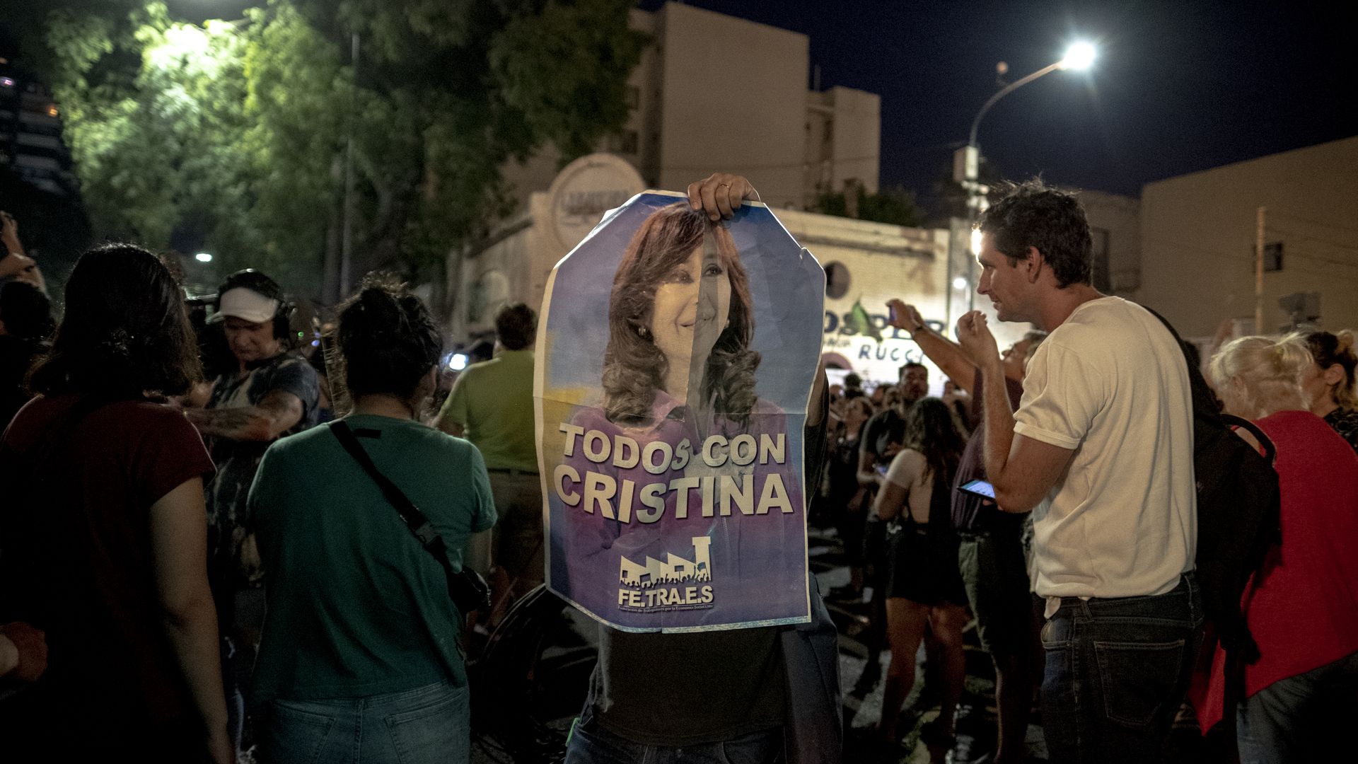 A supporter holds up a blue poster of Cristina Fernández de Kirchner that says "we are all with Cristina" in Spanish