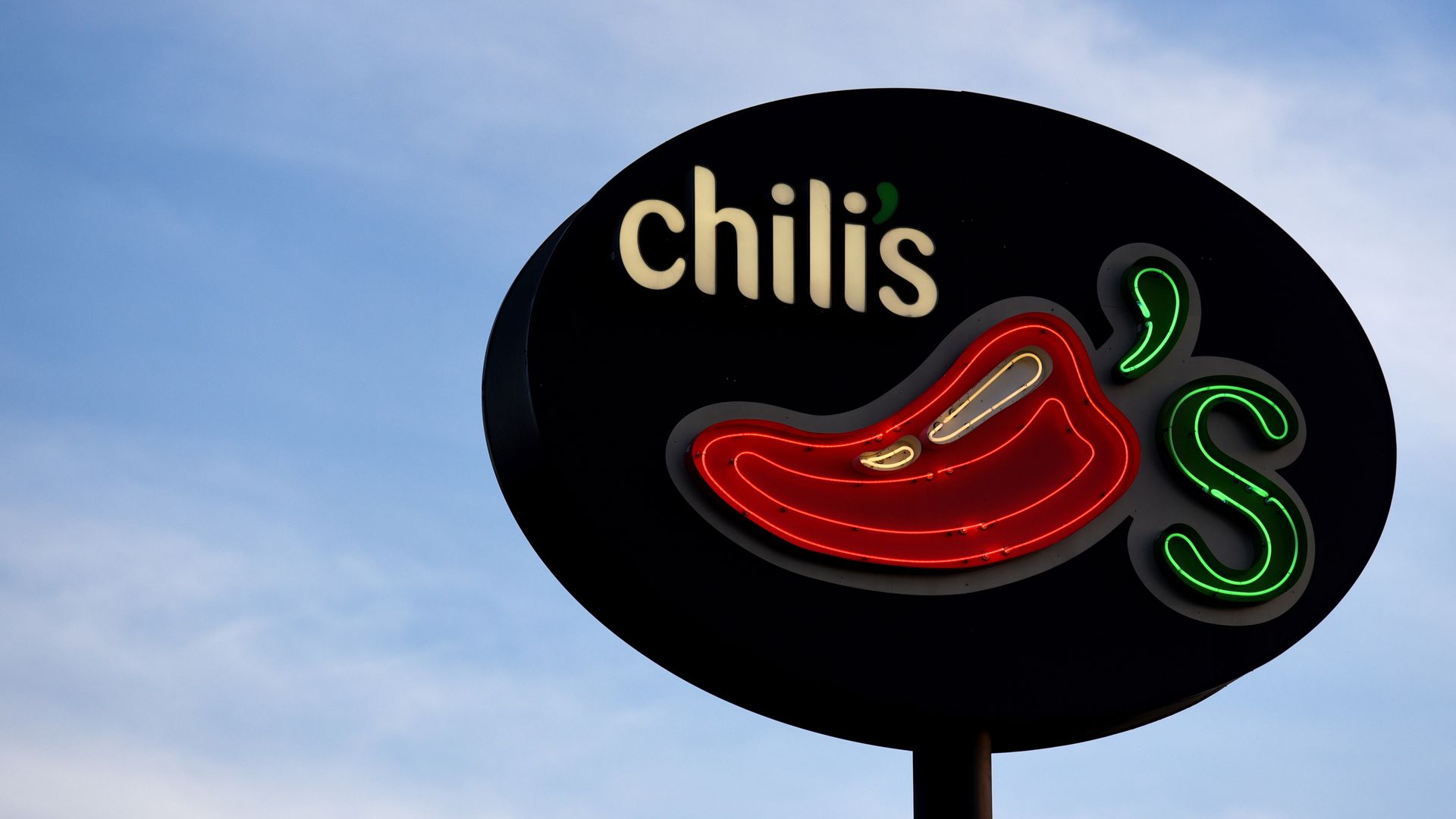 A photo of a Chili's sign against a cloudy blue sky