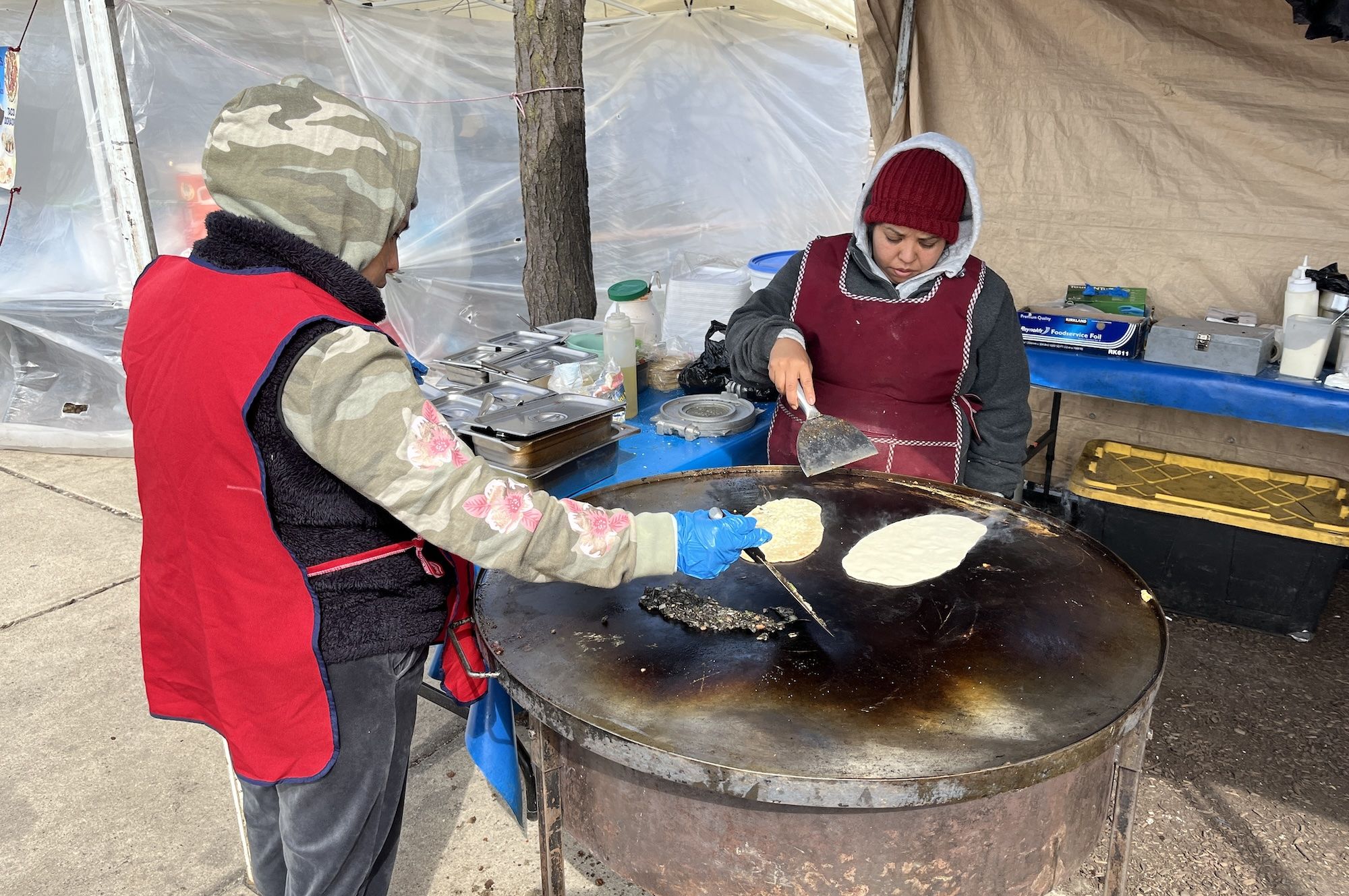 Two people pour corn masa on a griddle.