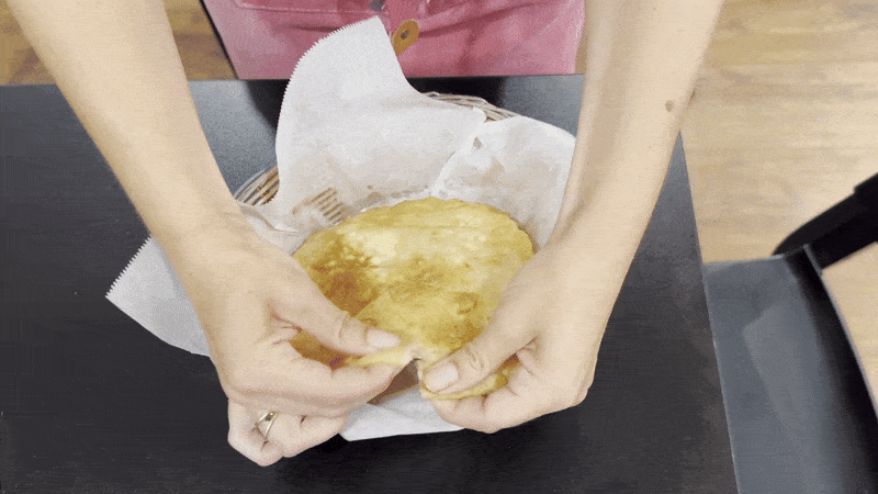 A pair of hands rips apart a circle of fried bread. Small white pieces of paneer can be seen inside.