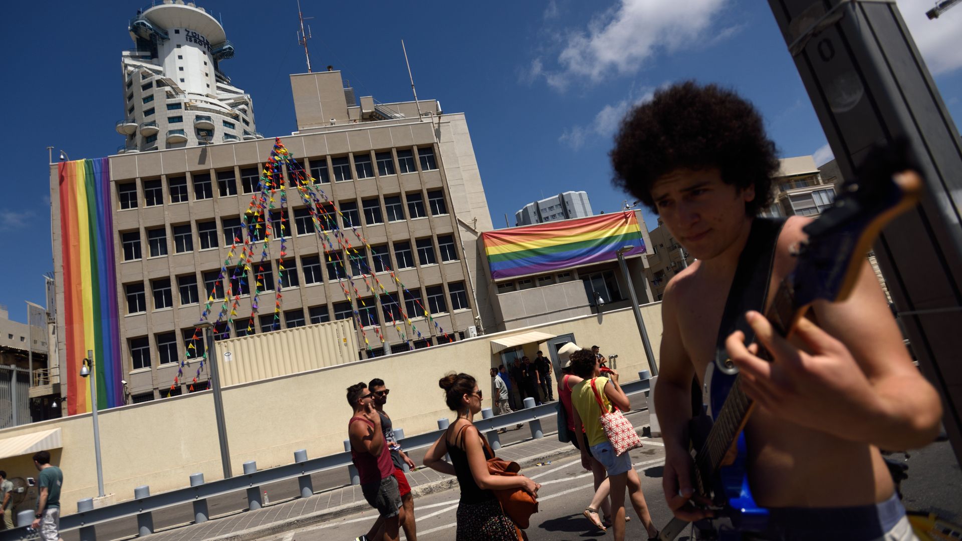 A person playing guitar in front of the American Emabssy in Tel-Aviv decorated with rainbow flags during a pride parade in 2015.