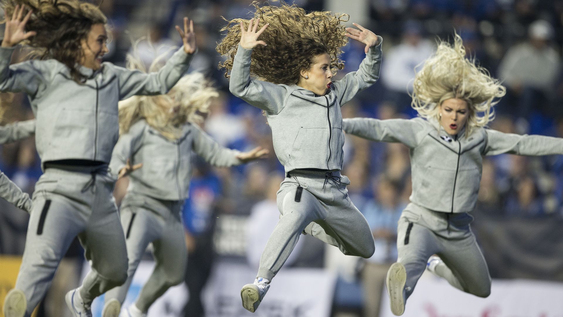 Women in gray sweatsuits leap in the air during a dance routine.